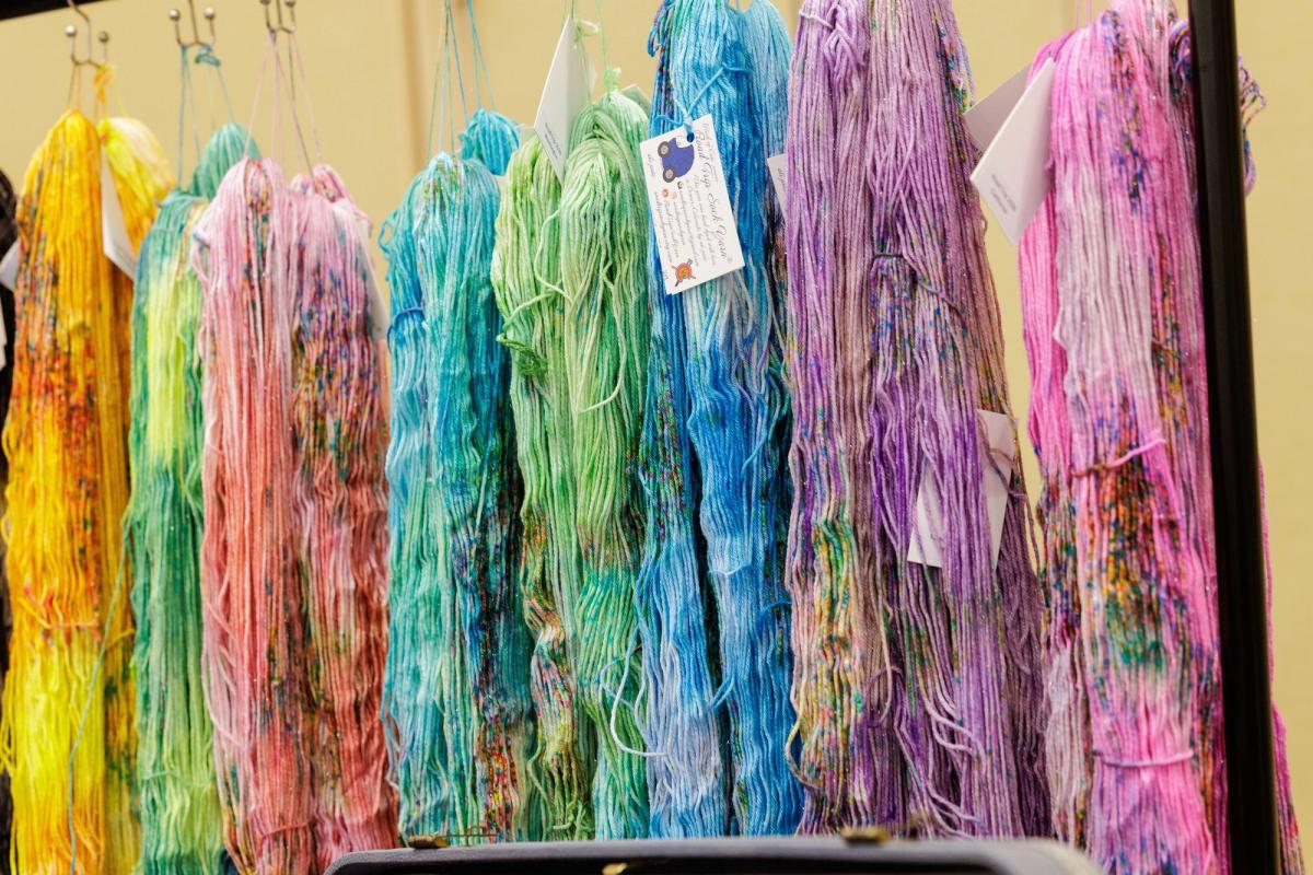 Colorful skeins of yarn in shades of yellow, green, blue, purple, and pink hang on display with tags attached.