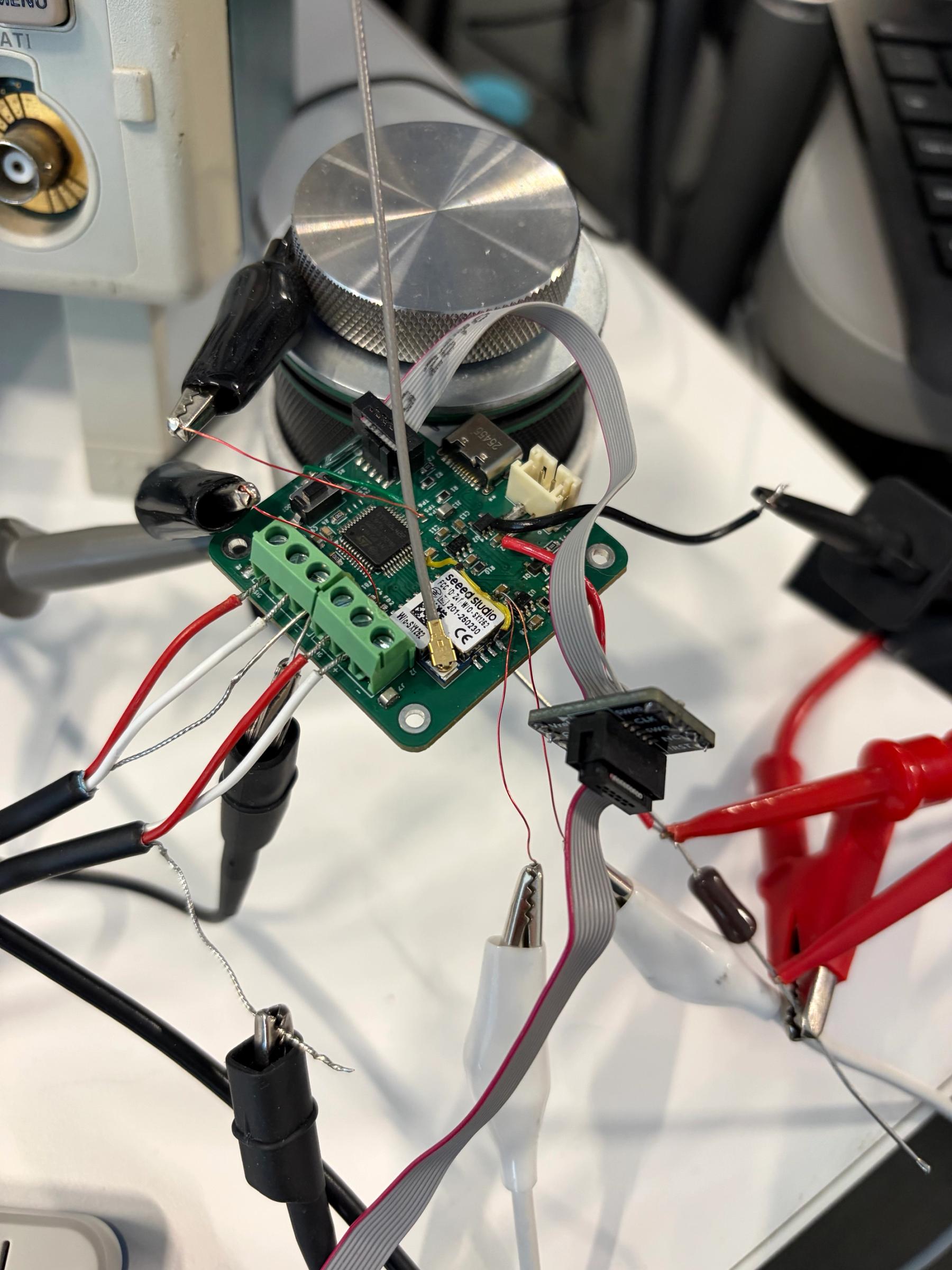 Close-up of an electronic circuit board connected to wires, probes, and testing equipment in a laboratory.