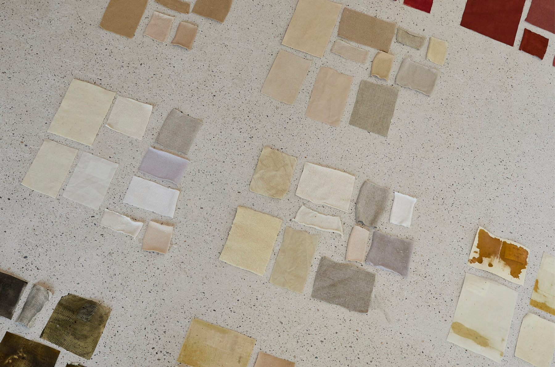 Assorted rectangular textile and material swatches in neutral, earthy, and rust tones arranged in clusters on a speckled work surface.