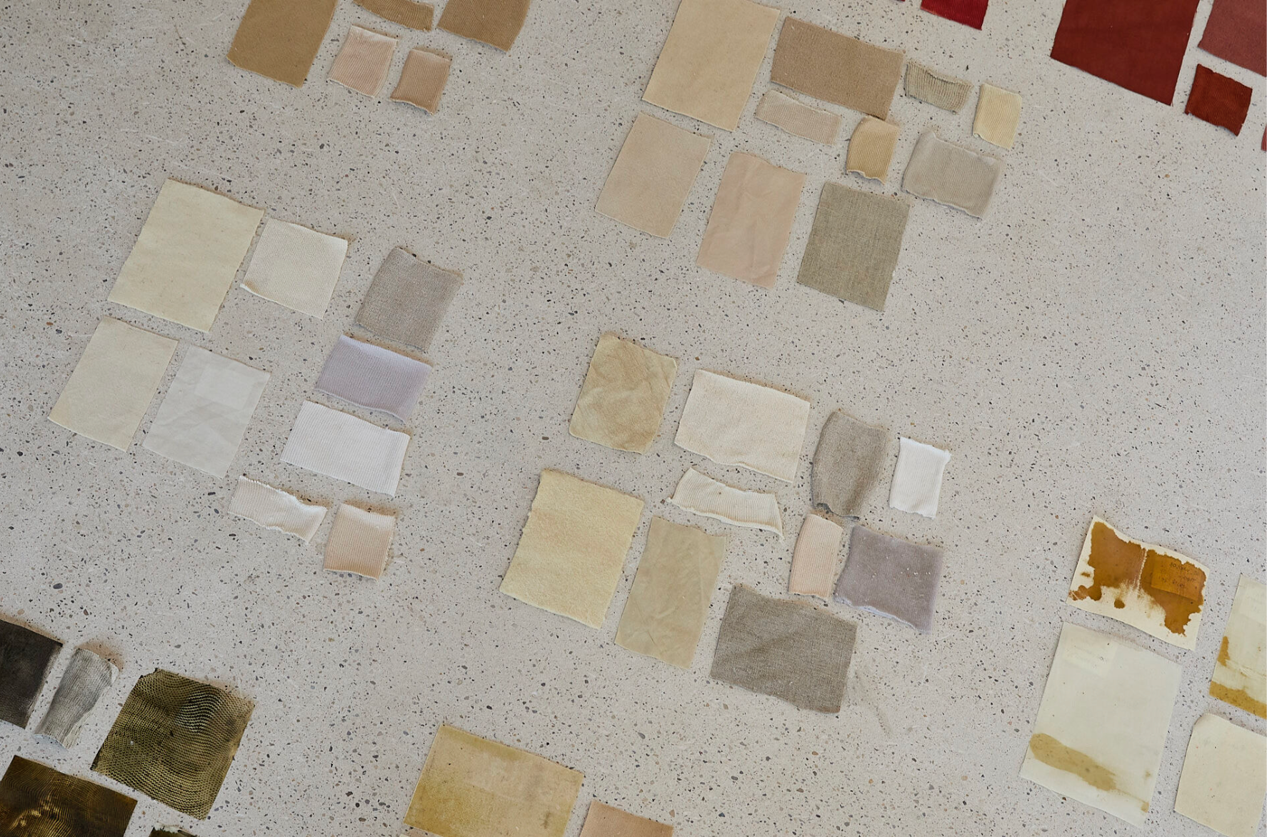 Assorted rectangular textile and material swatches in neutral, earthy, and rust tones arranged in clusters on a speckled work surface.