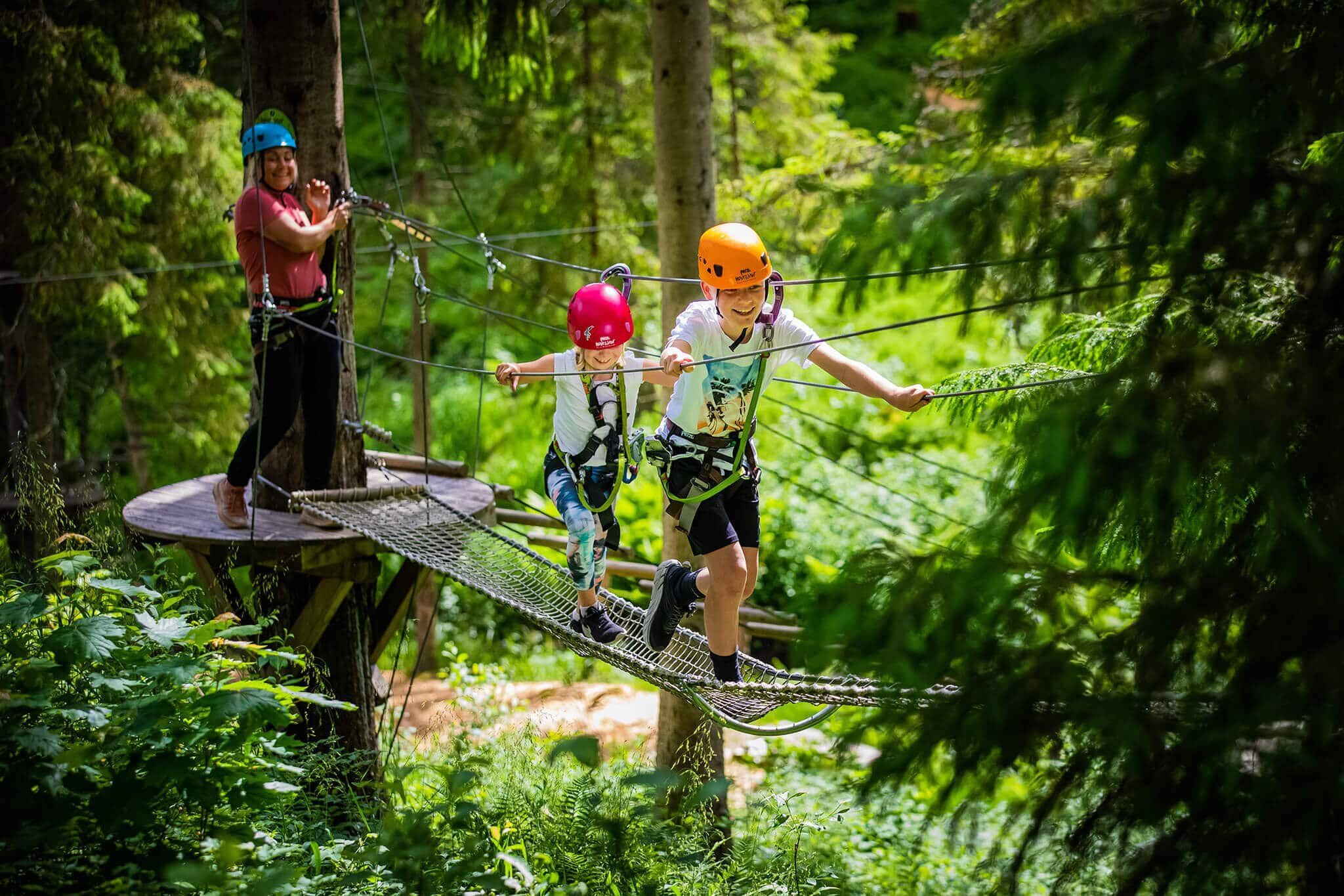 Barn med hjelm og klatresele balanserer på en hengebro i en klatrepark i skogen
