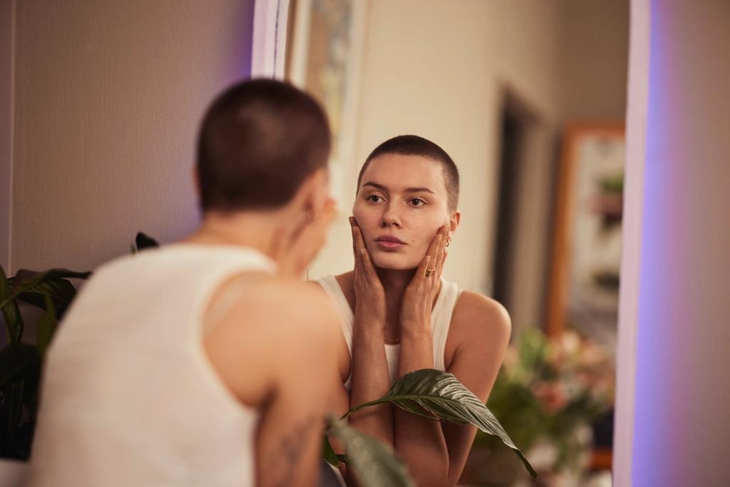 Kvinne holder seg til huden og ser seg i speilet