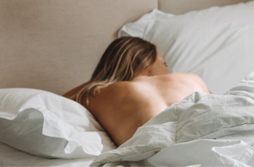 Kvinne som ligger i sengen med bar rygg