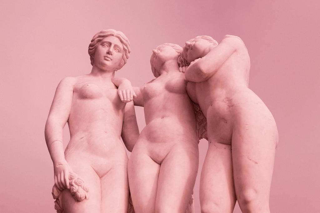 3 kvinnelige statuer i rosafarge som holder rundt hverandre