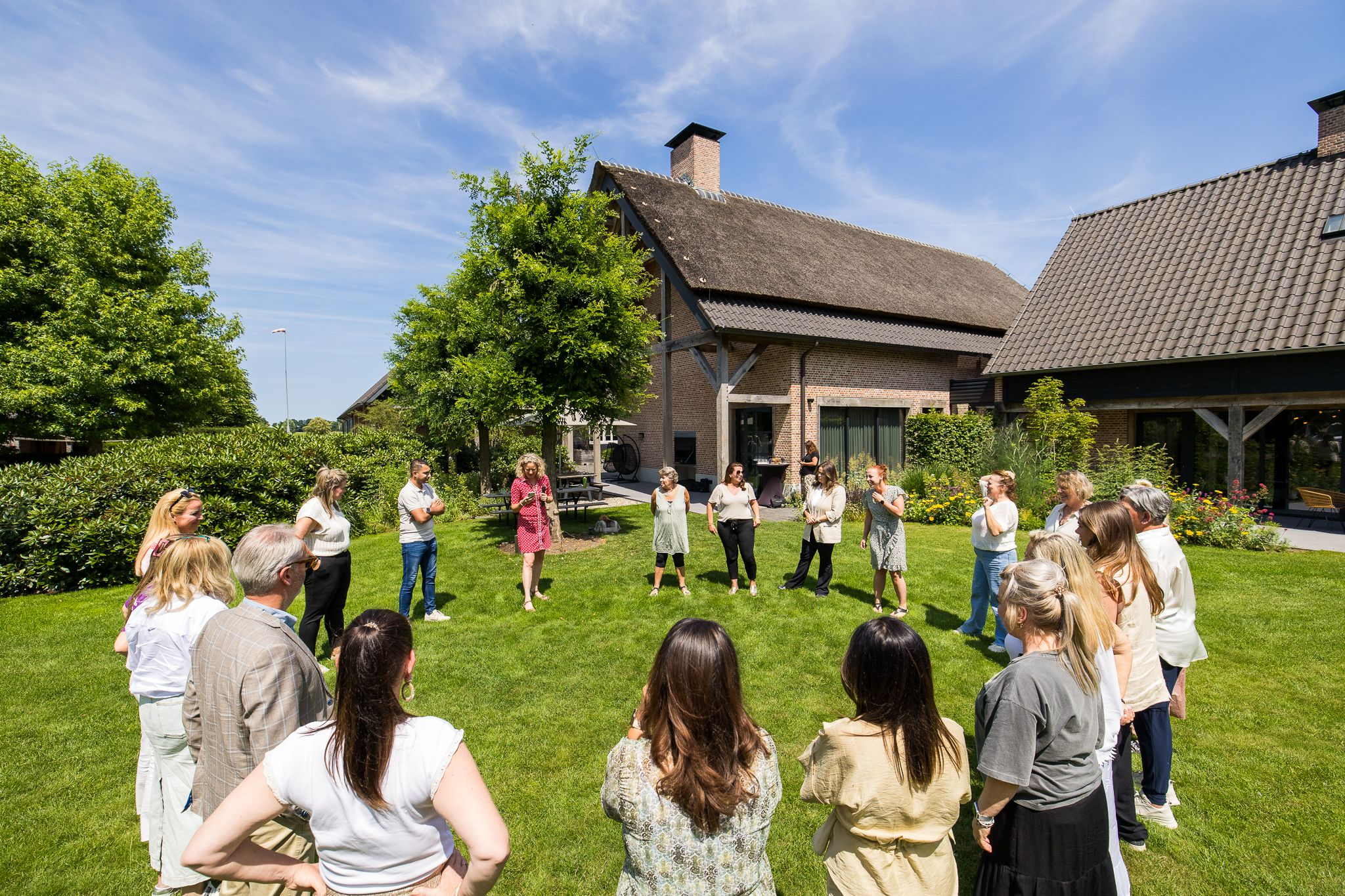 Groep collega’s in een kring op het gazon voor een landhuis