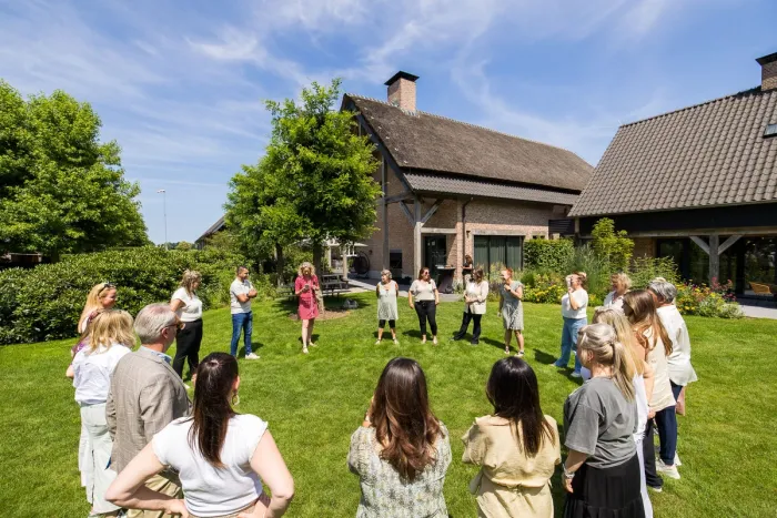 Groep collega’s in een kring op het gazon voor een landhuis
