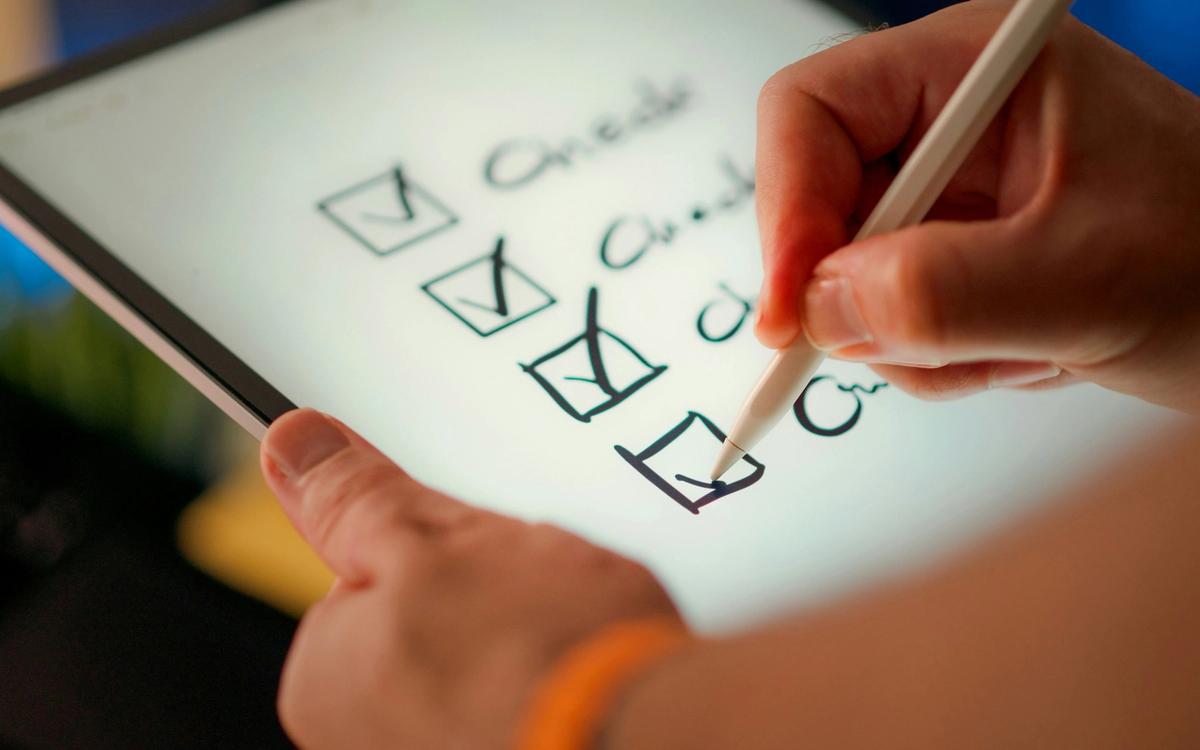 Hand setzt auf einem Tablet Häkchen in eine Checkliste