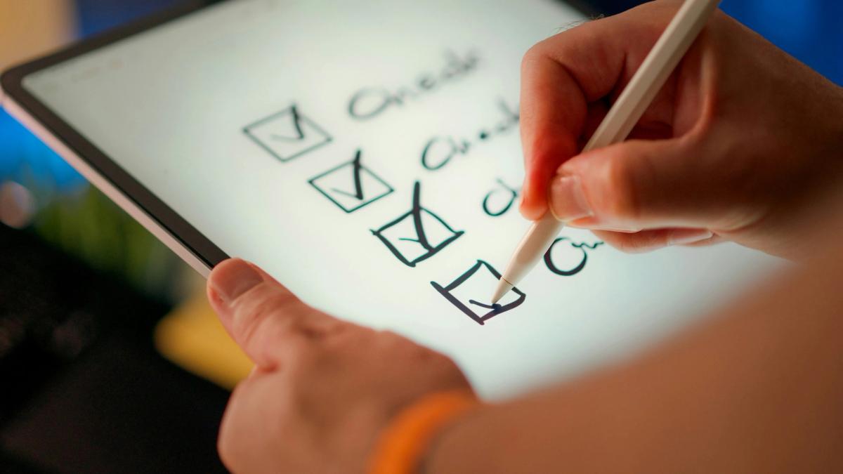 Hand setzt auf einem Tablet Häkchen in eine Checkliste