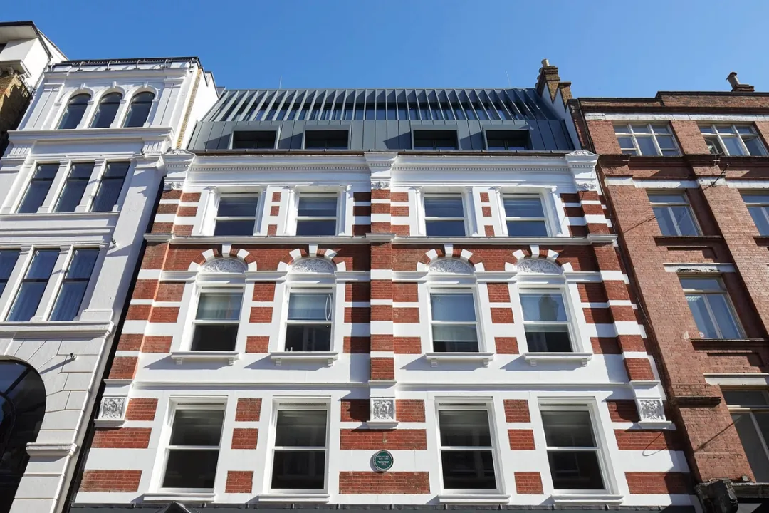 View looking upwards at a red brick building with a triple height mansard roof and white window frames 