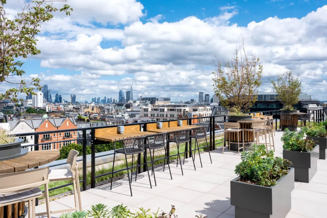 Planters and bar seating on a paved roof terrace overlooking London's skyline