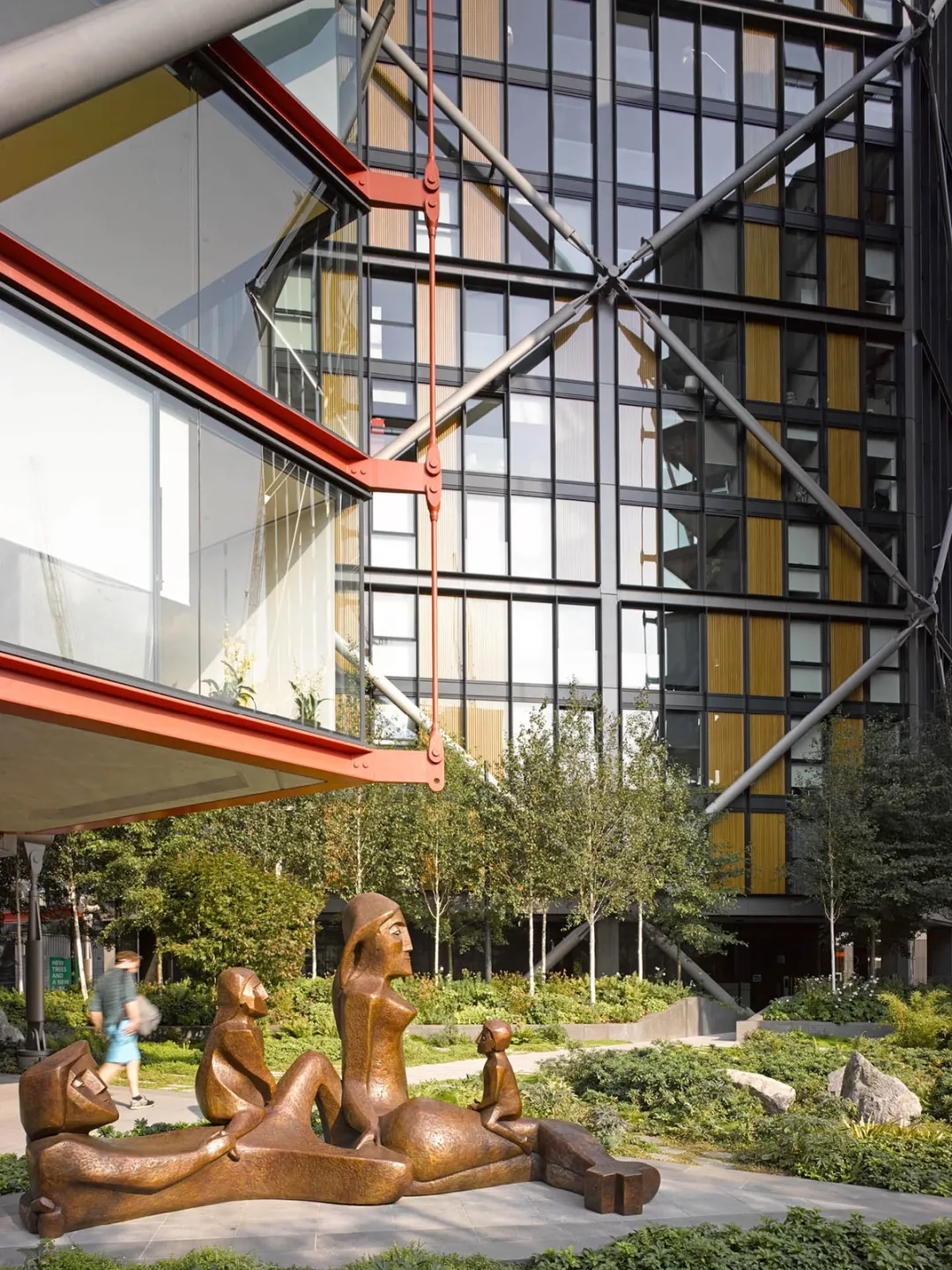 A large bronze sculpture of people sat on floor surrounded by green planting and residential towers