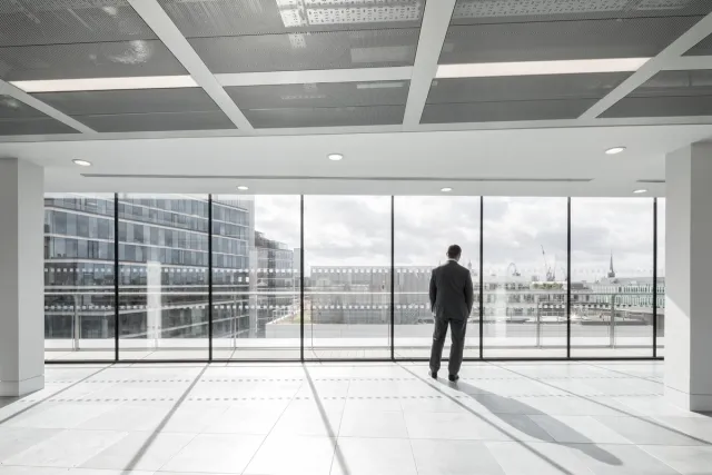man looking through window in empty office with no furniture and view of London