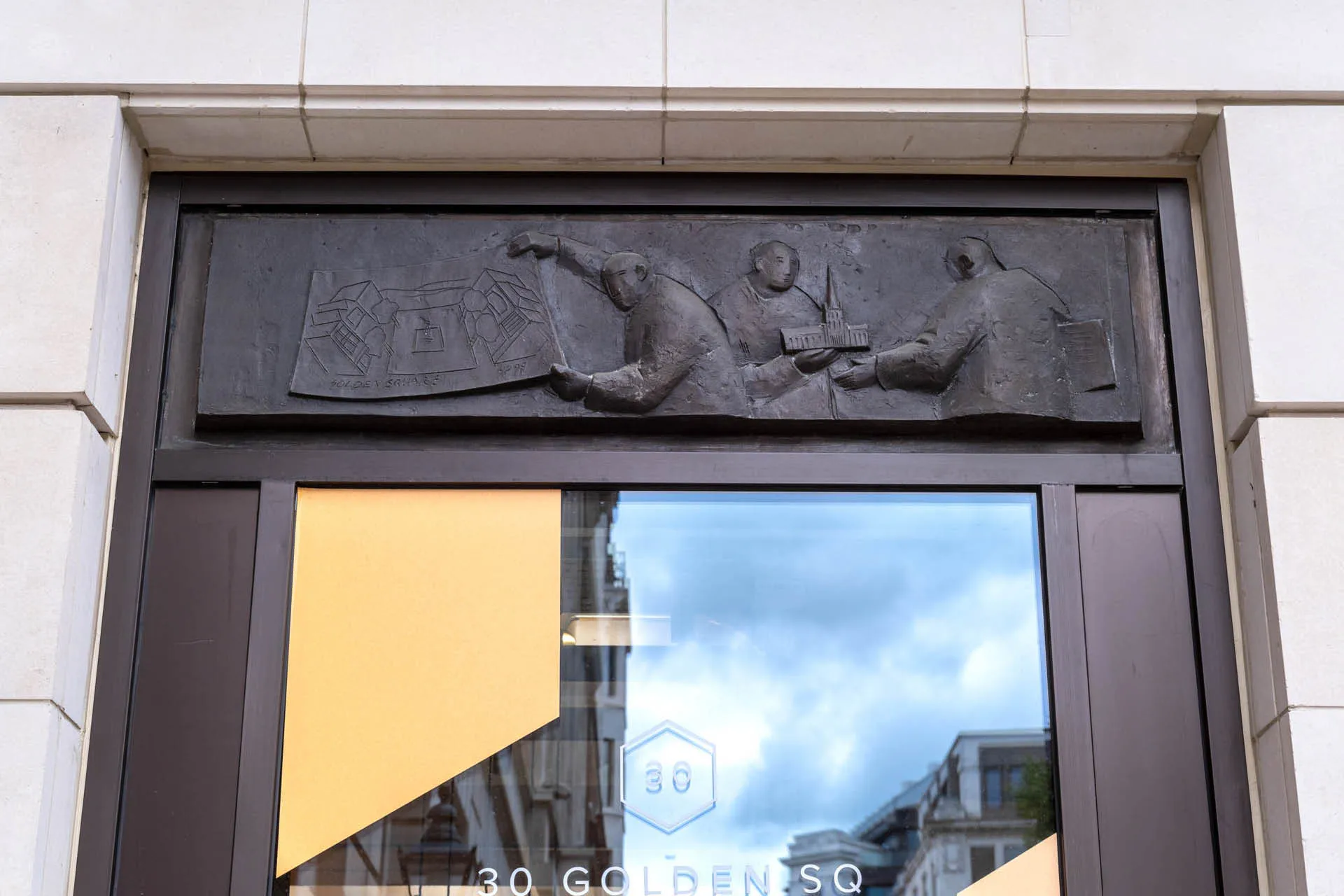 Close up of bronze casting above a window of figures holding plans and building models