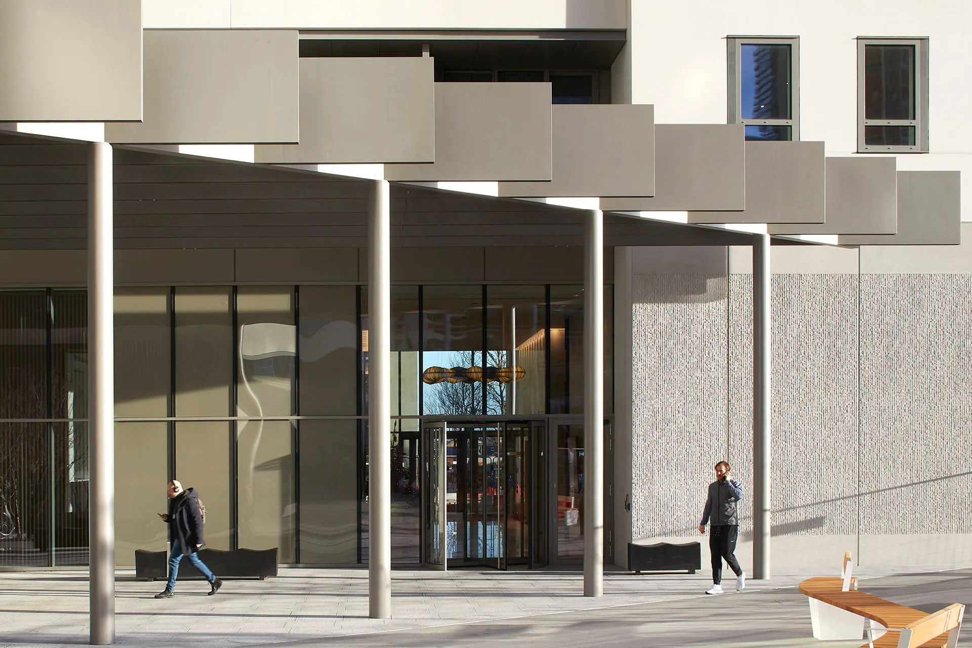Entrance pavilion to white building with two people walking past