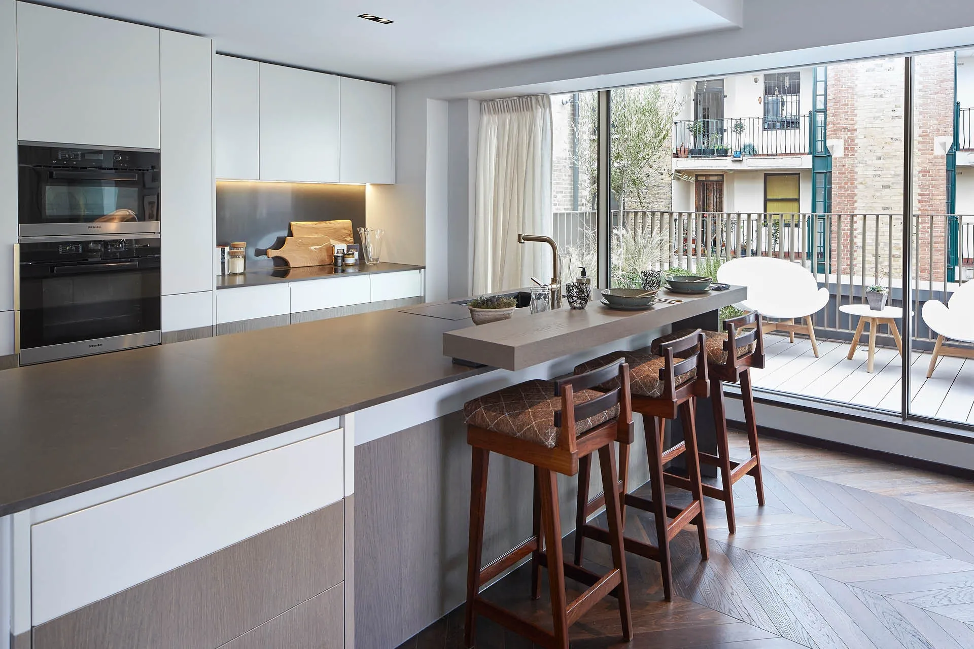 A kitchen island with bar stools and a balcony beyond