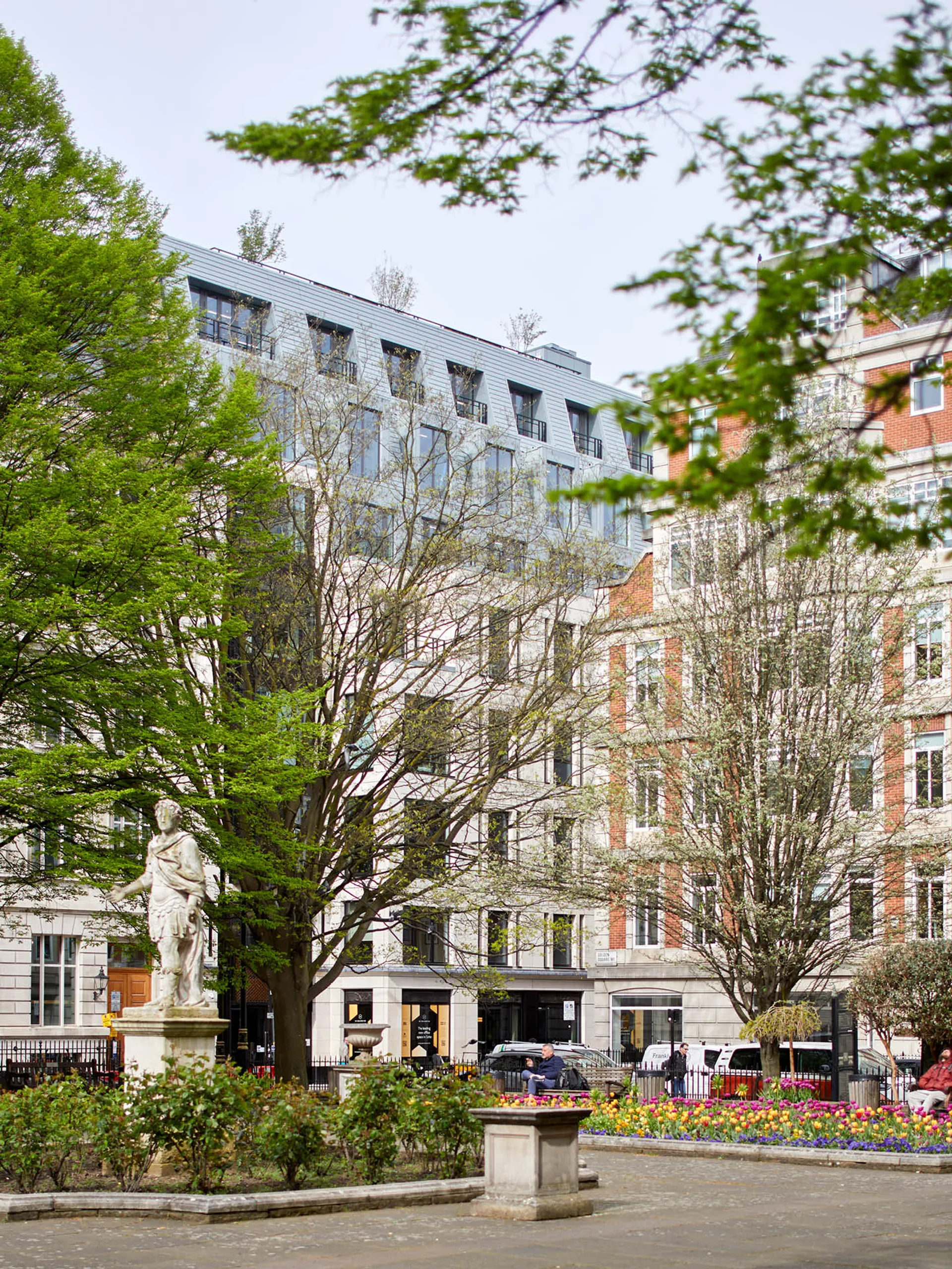 A view across the landscaped Golden Square with a statue, tall office building visible in the distance