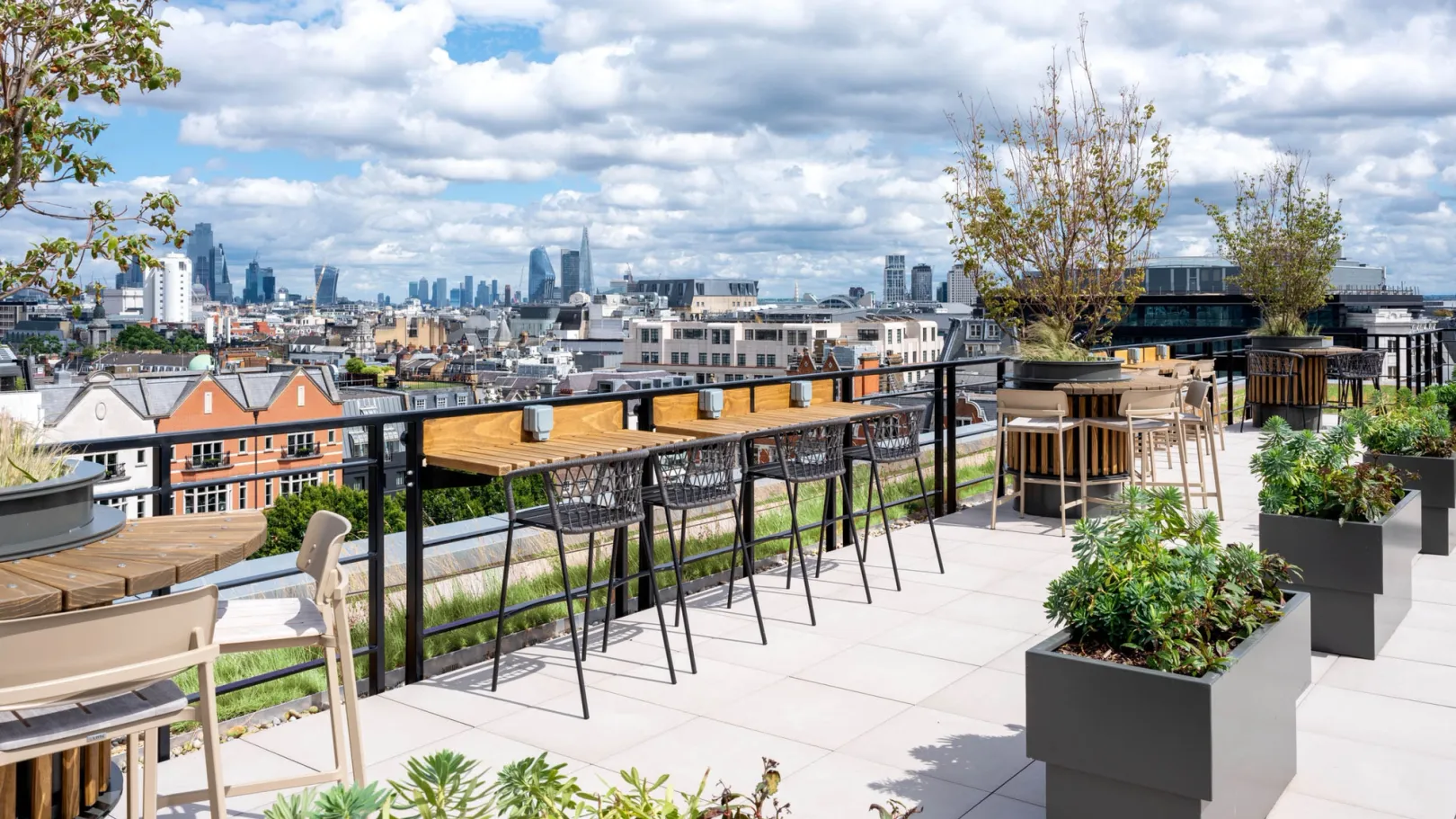 A paved roof garden with trees and shrubs, bar seating overlooking London skyline