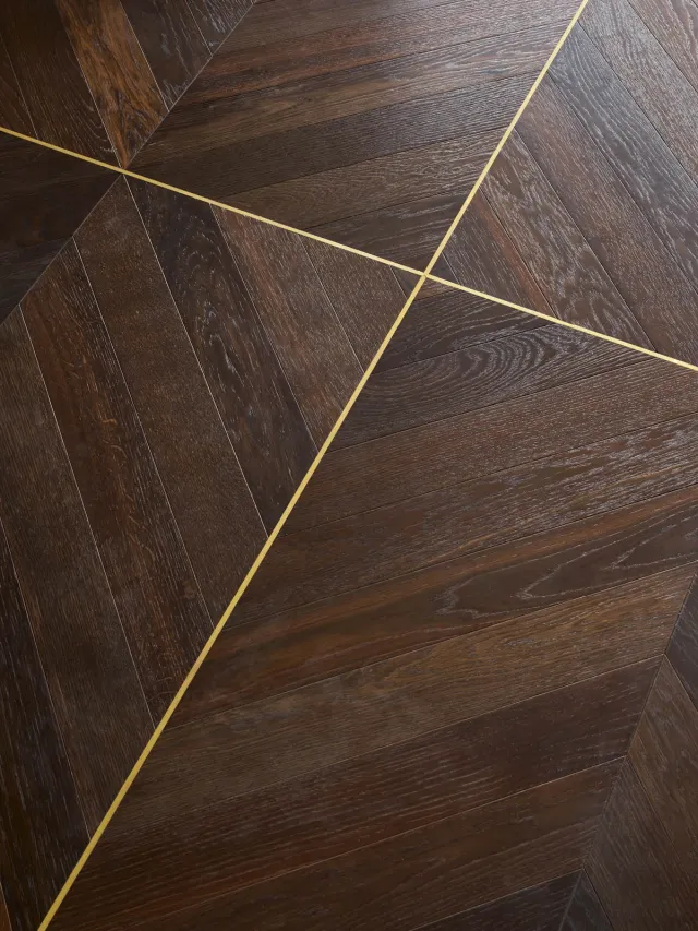 Dark brown wood herringbone flooring inlaid with brass lines