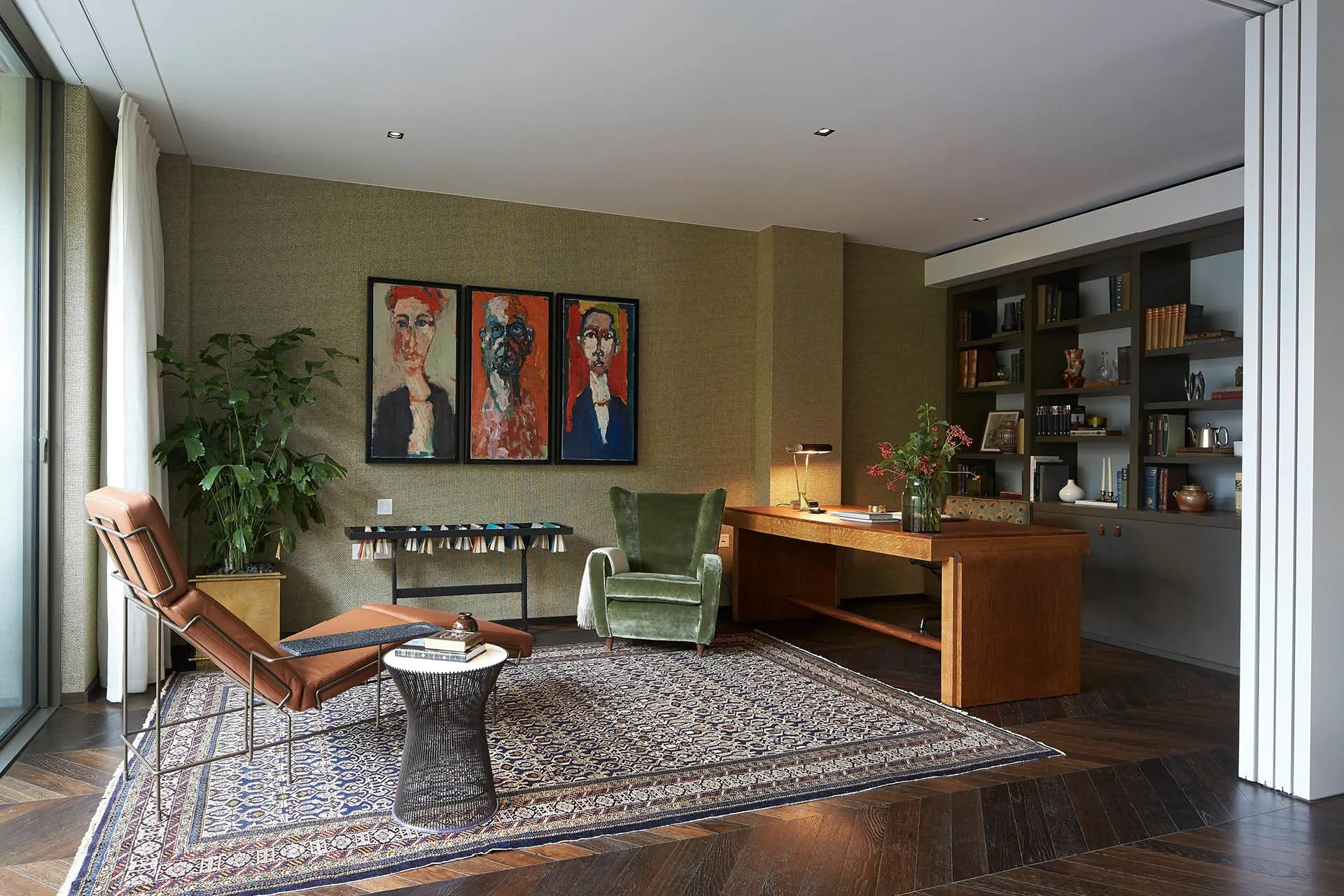 A dark green study with large desk and paintings on the wall