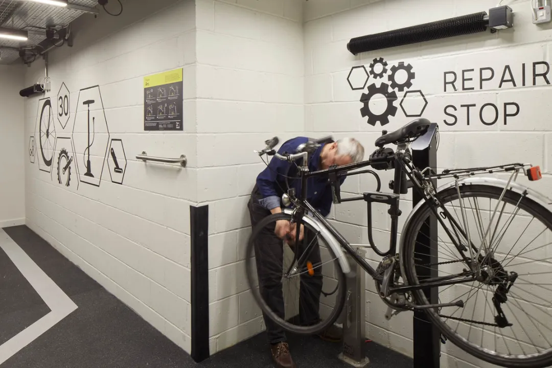A man repairing a bicycle on a stand in front of a wall reading 'Repair Stop'