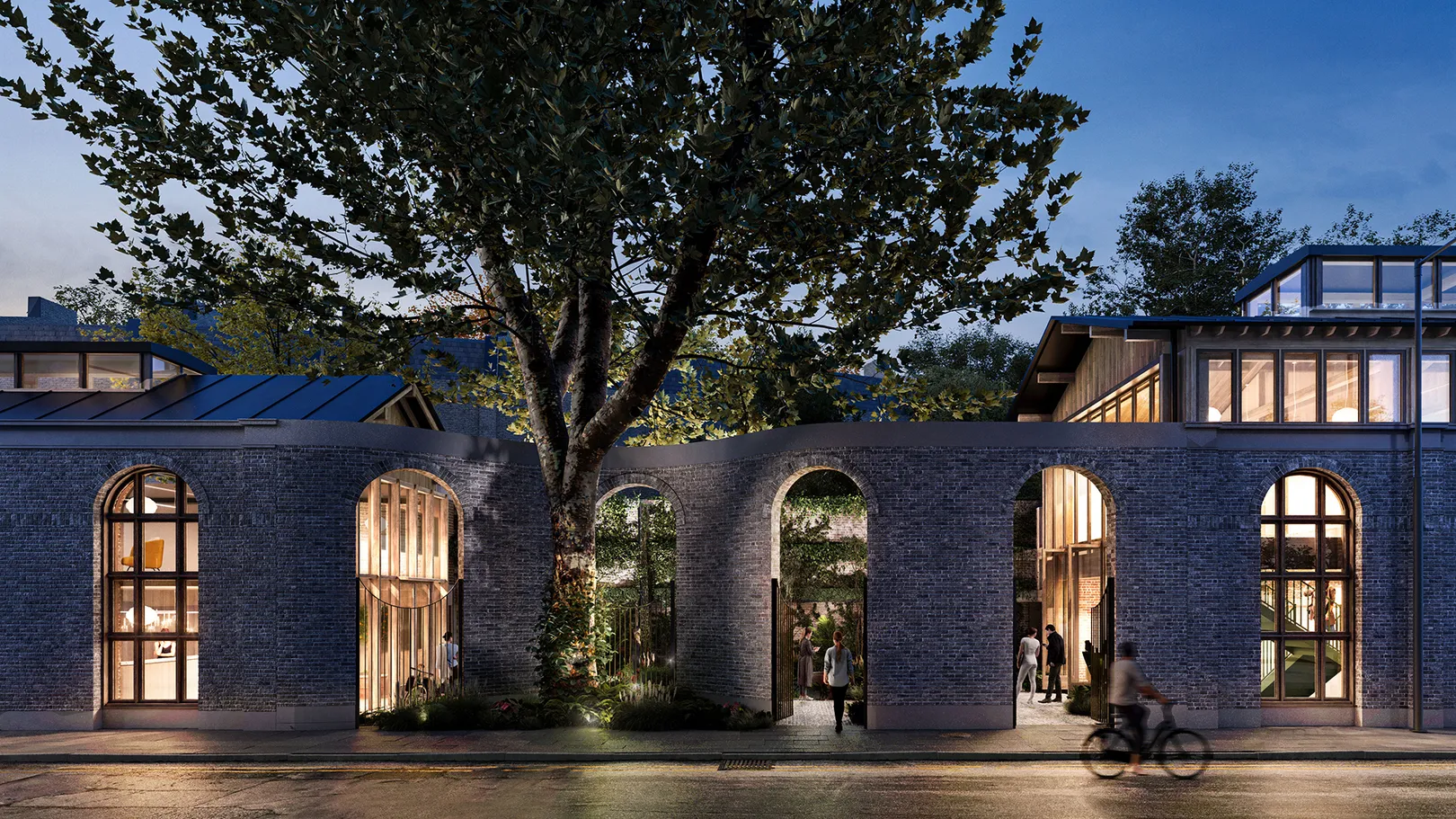Arches alongside street at night with lit up building visible through the arches with road and tree in foreground
