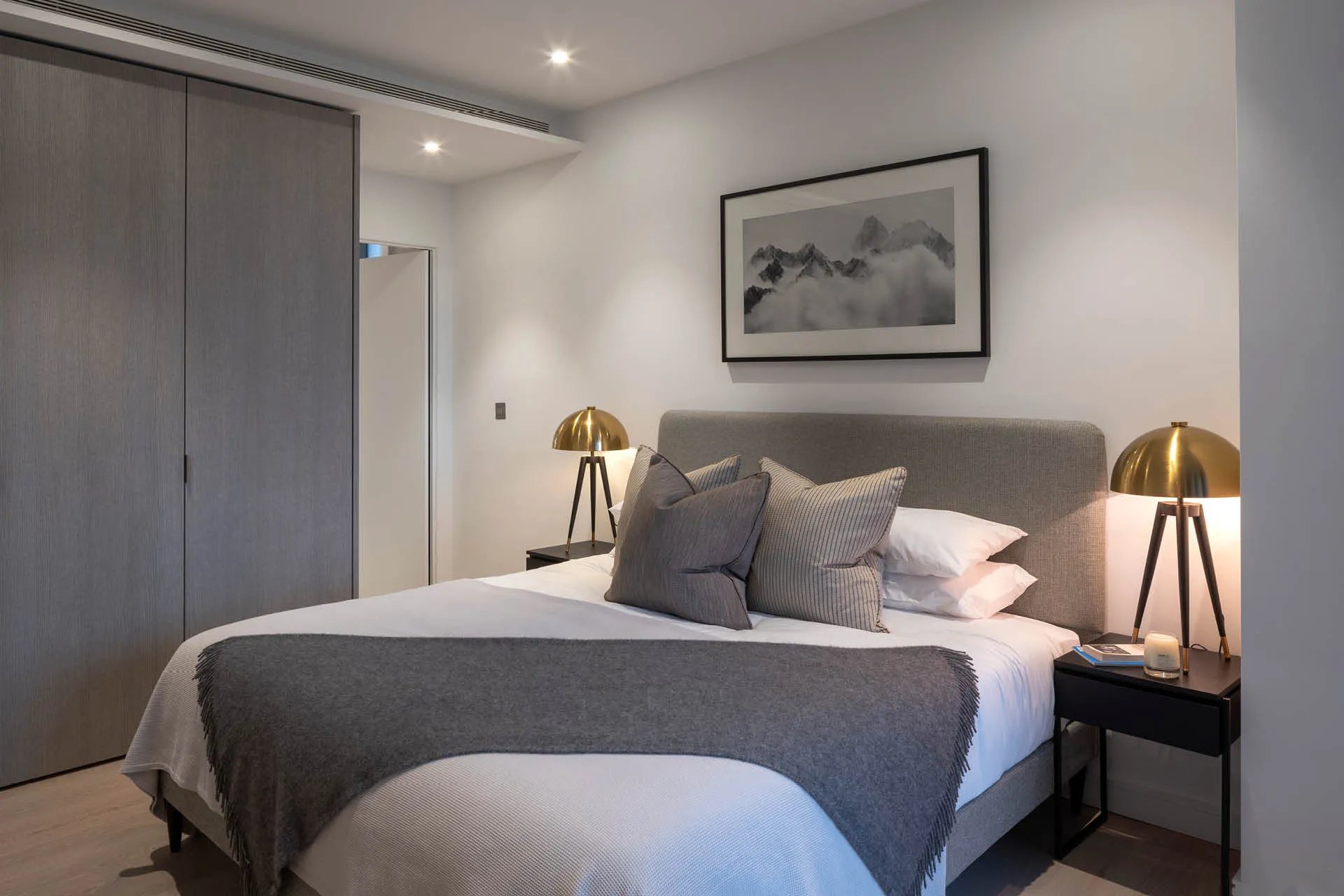 A bed with grey covers and gold lamps either side