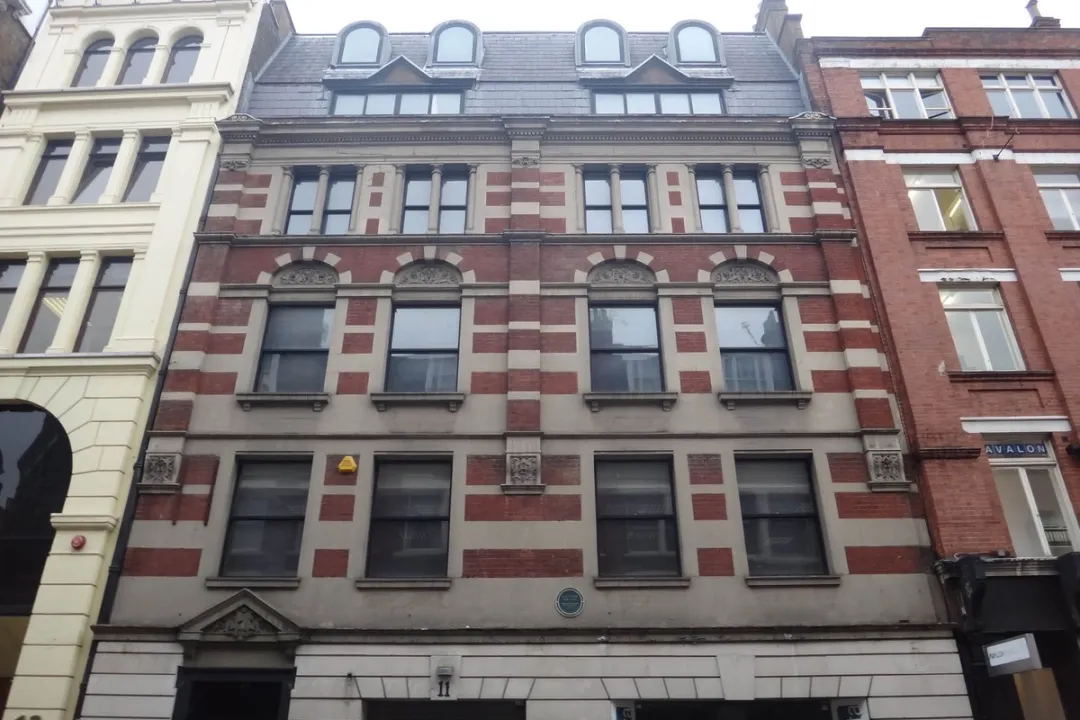 View looking up at a 6 storey brick building with discoloured stone and darkened windows