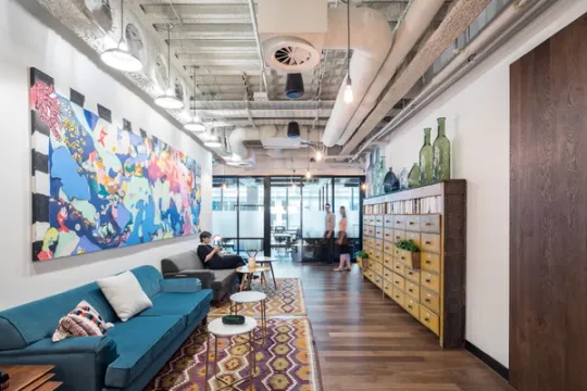 Two sofas side by side with a large colourful painting behind and glass partitioned meeting rooms to the side