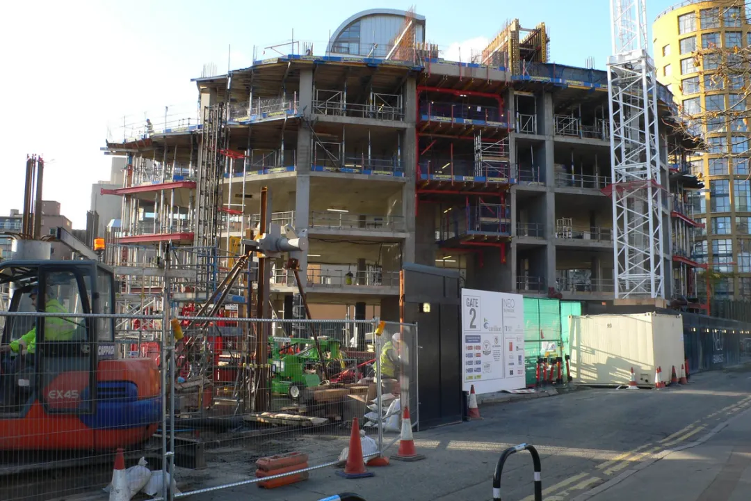 A concrete shell of a residential tower with 5 storeys built and hoarding around base
