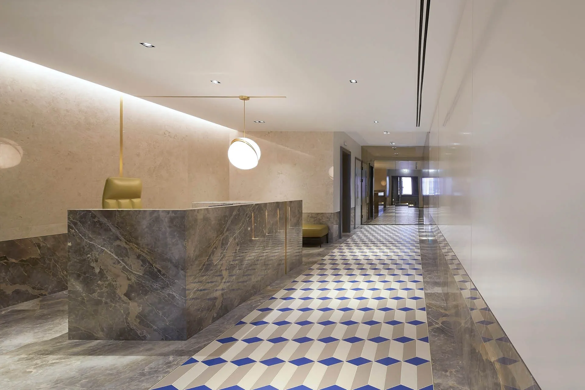 A long reception hall with large marble desk and geometric blue and beige tiled floor