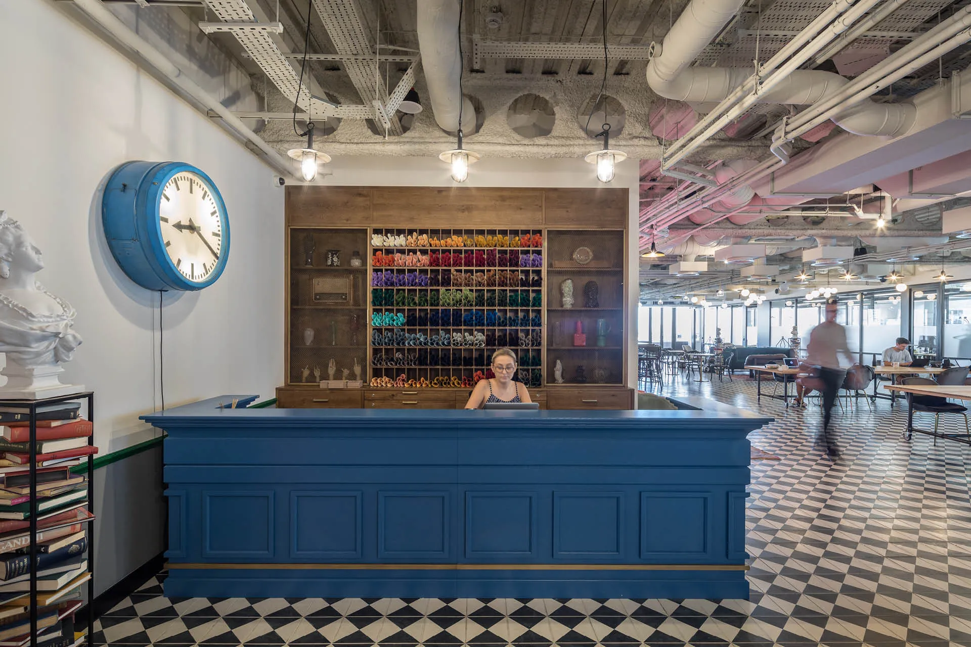 Blue reception desk next to large clock, hot desks in the background