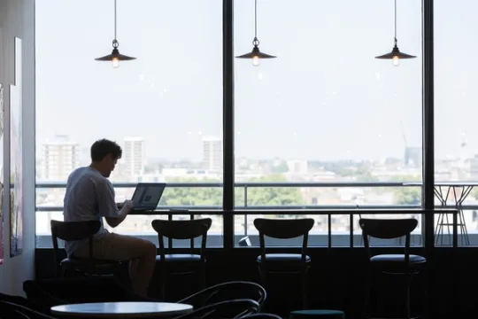A person sits at a window using a laptop