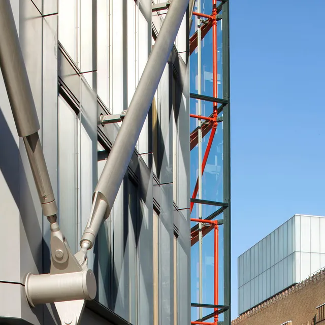 Close up of steel cross-bracing with glass external lift, Tate Modern roof in background