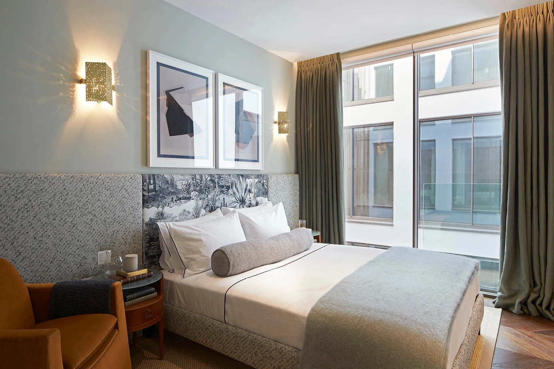 A bedroom with a bed in the centre, grey blankets and curtains and an orange armchair