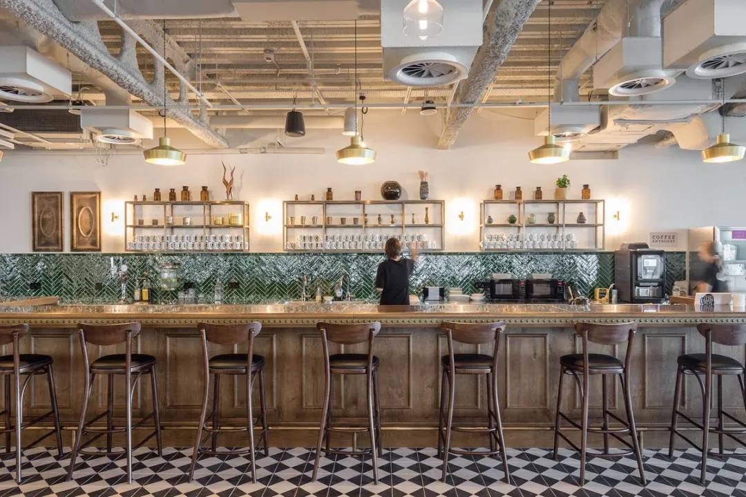 A wooden office kitchenette with people sat at high stools