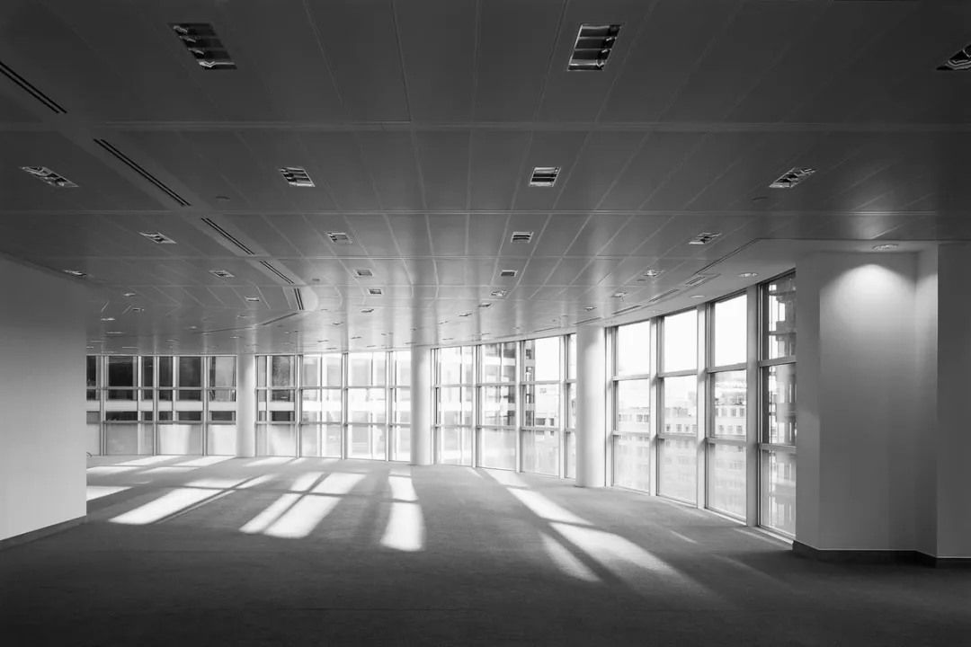 Black and white photo of original office floor with carpeted floors and floor to ceiling windows around the curved parameter 