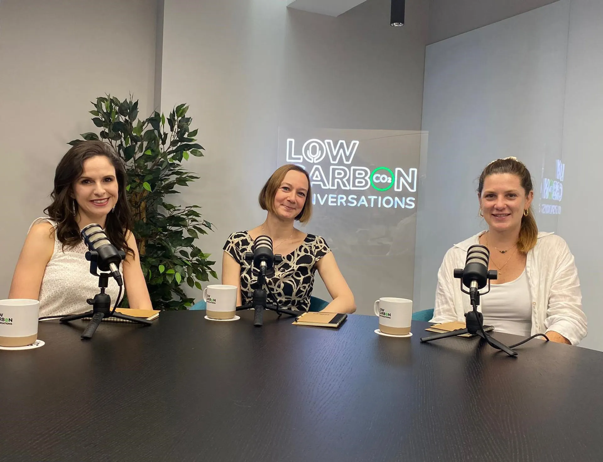 Anya Schellenbauer at table behind microphone with two speakers