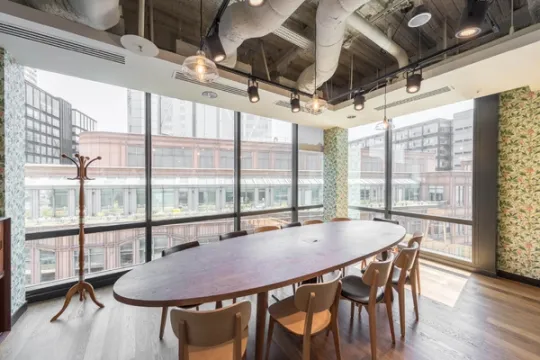 An oval wooden meeting desk surrounded by chairs next to a large window