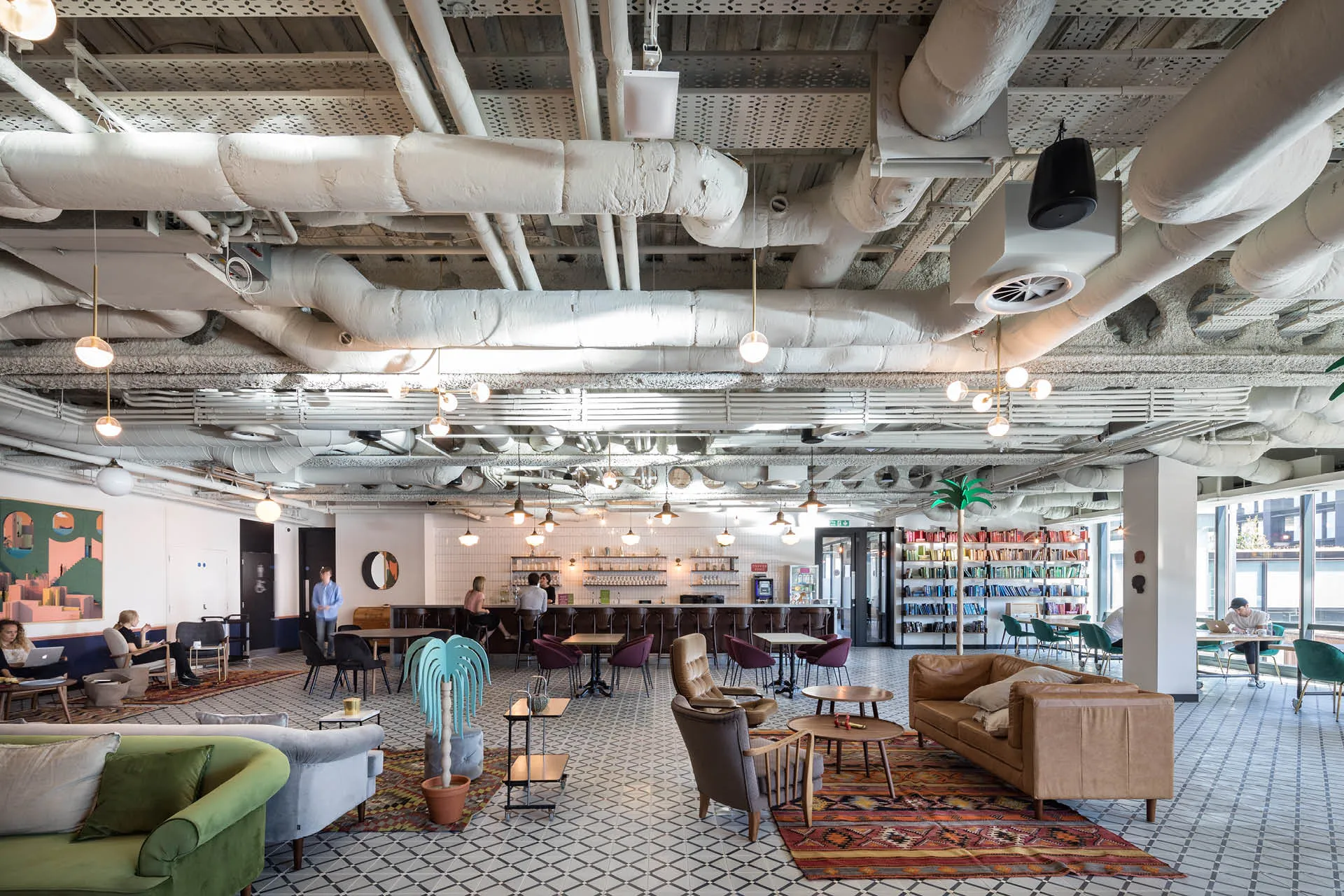 A wide view of a spacious co-working space with break out sofa seating, a bar kitchenette and library in the background