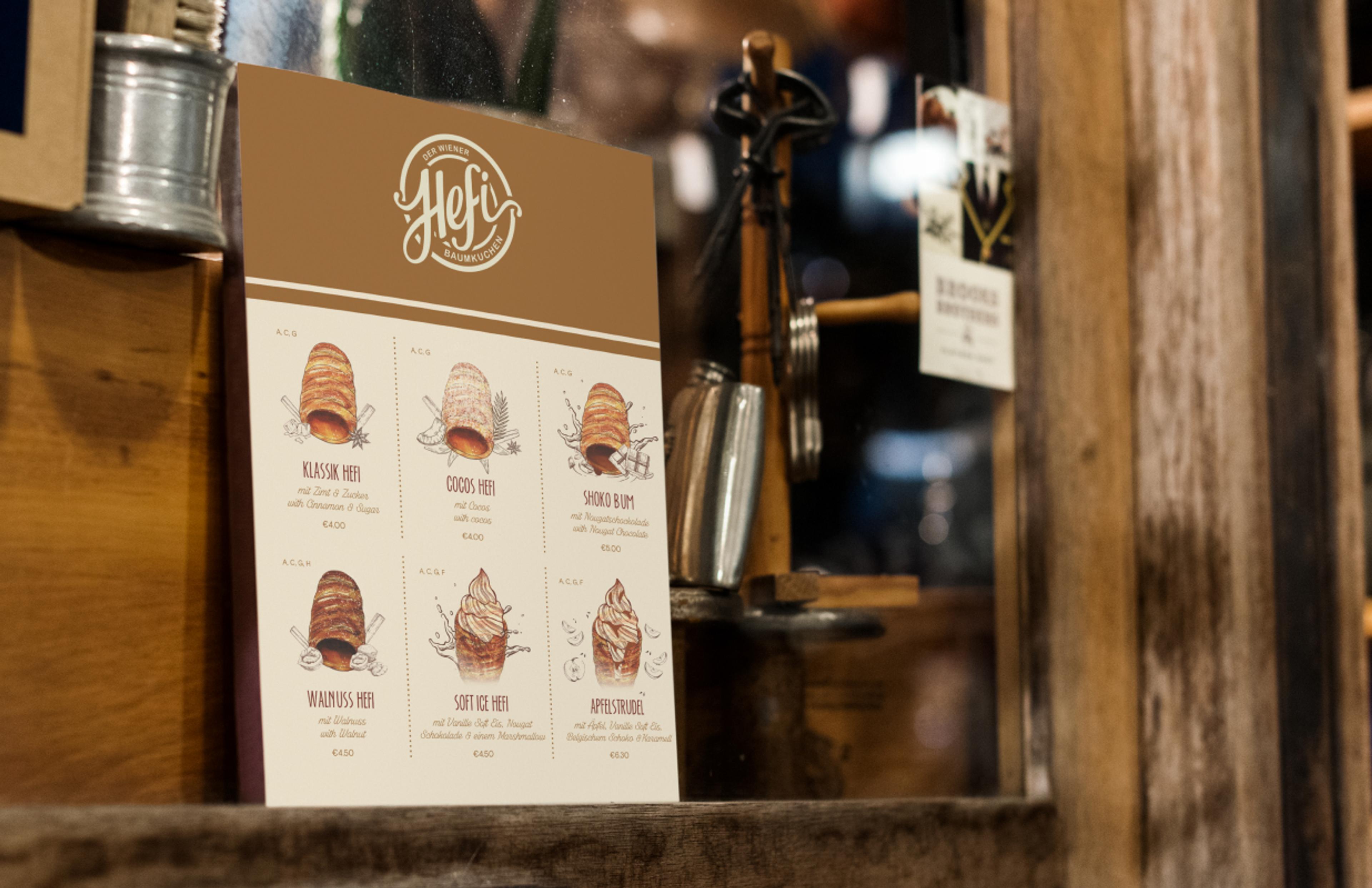 Eine Speisekarte mit illustrierten Baumkuchen-Sorten, präsentiert vor einem Fenster mit Holzrahmen.