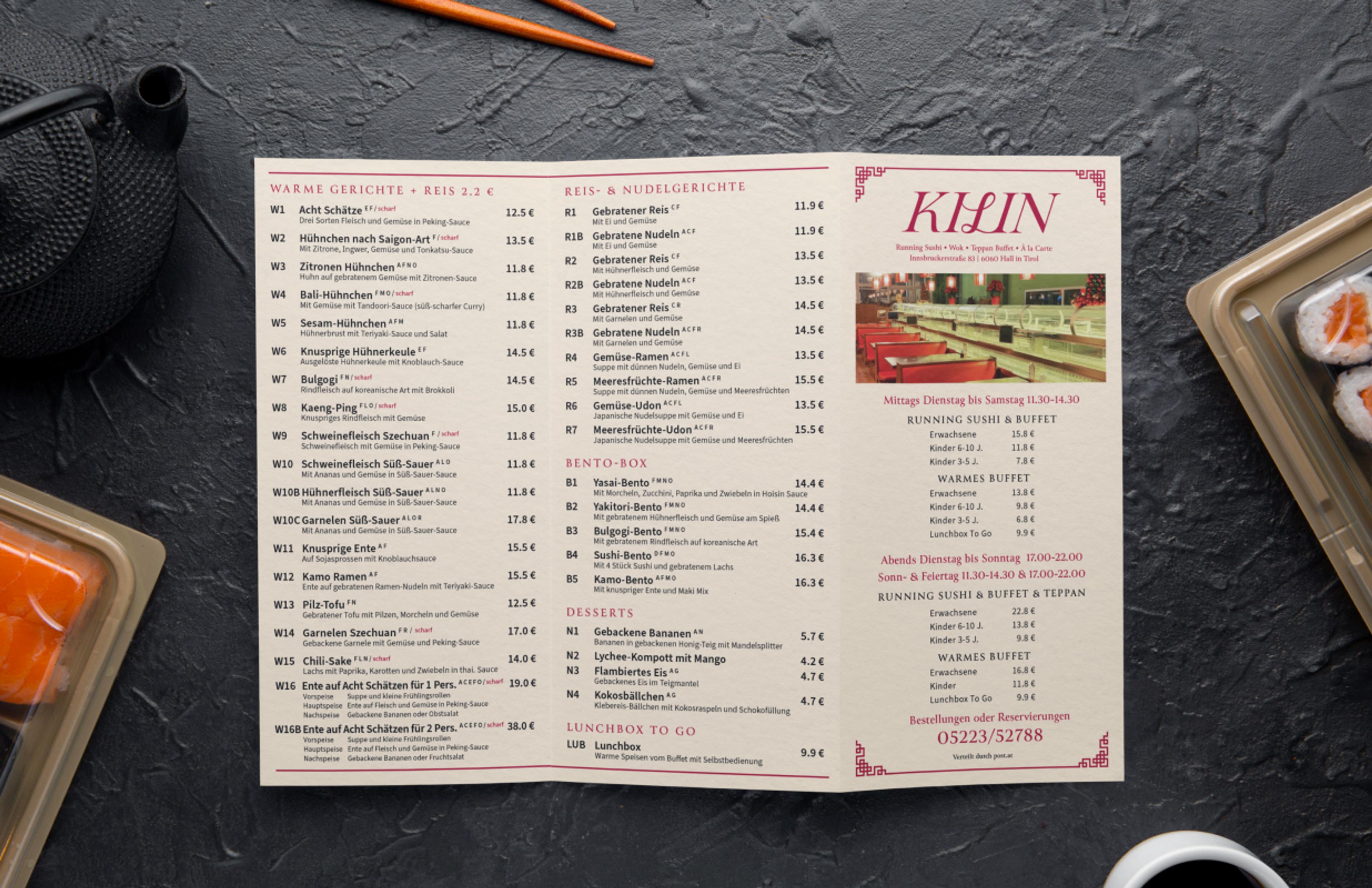 Hochwertiger Restaurant-Flyer des Kilin Restaurants, stilvoll platziert neben Sushi, Algensalat und Sojasauce. Edles Design in Rot und Gold mit asiatischen Mustern, kombiniert mit traditionellen Gerichten. Perfektes Beispiel für modernes Gastronomie-Marketing und erstklassige visuelle Identität. Gestaltung von Unerwartet Branding und Design OG aus Graz, Österreich.