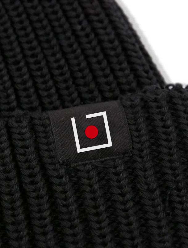 Ijob-Logo auf einer schwarzen Strickmütze – Eine Nahaufnahme eines schwarzen Beanies mit einem gestickten Ijob-Logo-Tag. Das Logo zeigt ein weißes Quadrat mit einem roten Punkt in der Mitte.