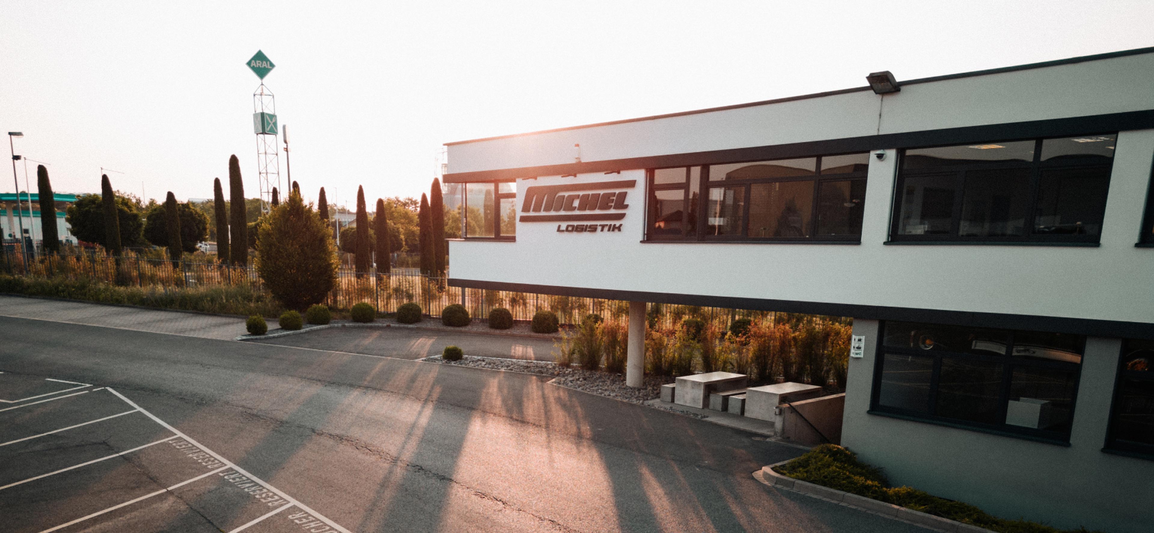 WOODS Consulting, Leopold Michel GmbH Michel Logistik Hauptgebäude bei Sonnenuntergang, mit Branding-Elementen – Design und Markenentwicklung von Unerwartet Design.