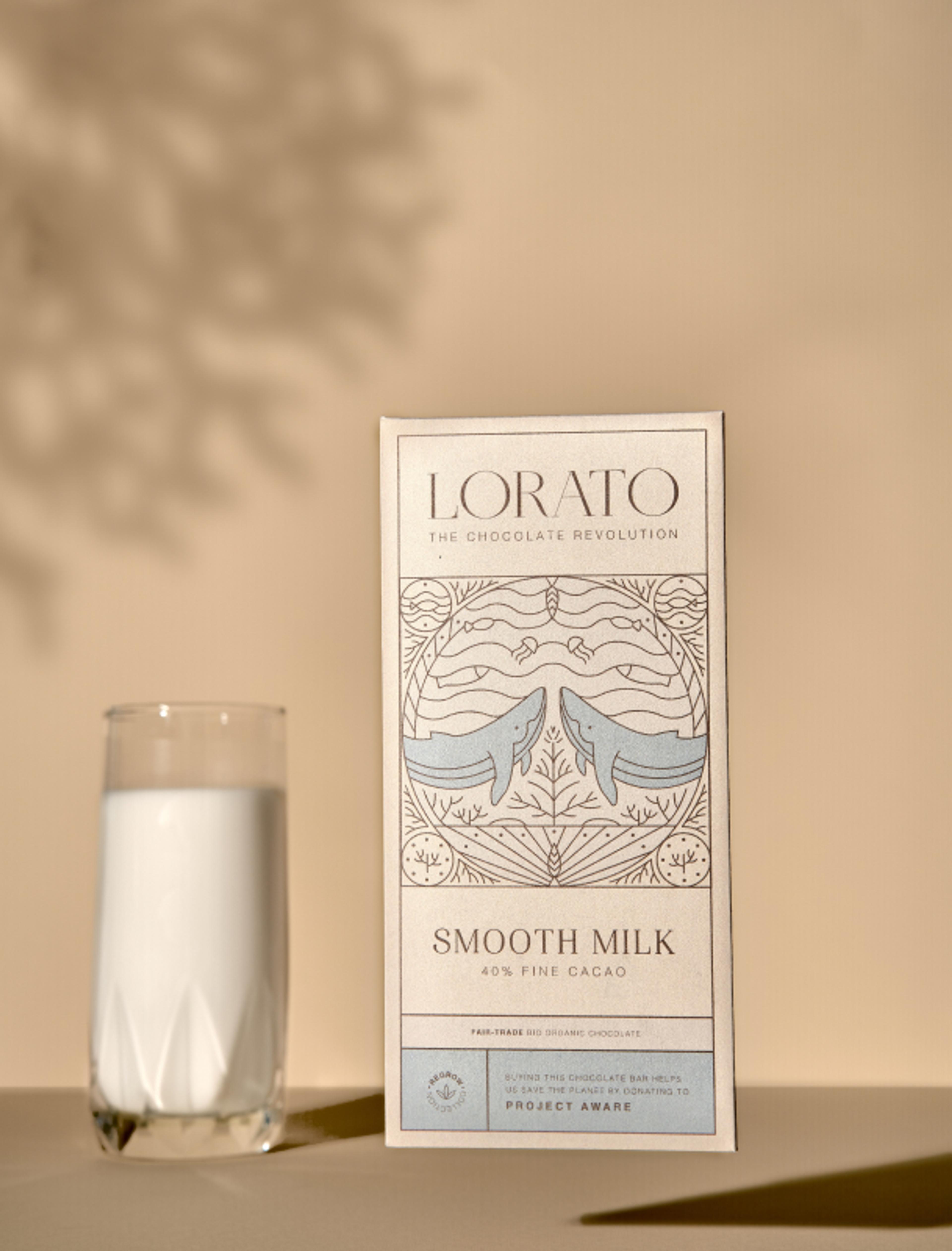 Lorato Smooth Milk Schokoladenverpackung mit handgezeichneten Walen, 40 % feiner Kakao. Neben der Schokolade steht ein Glas Milch auf beigem Hintergrund.