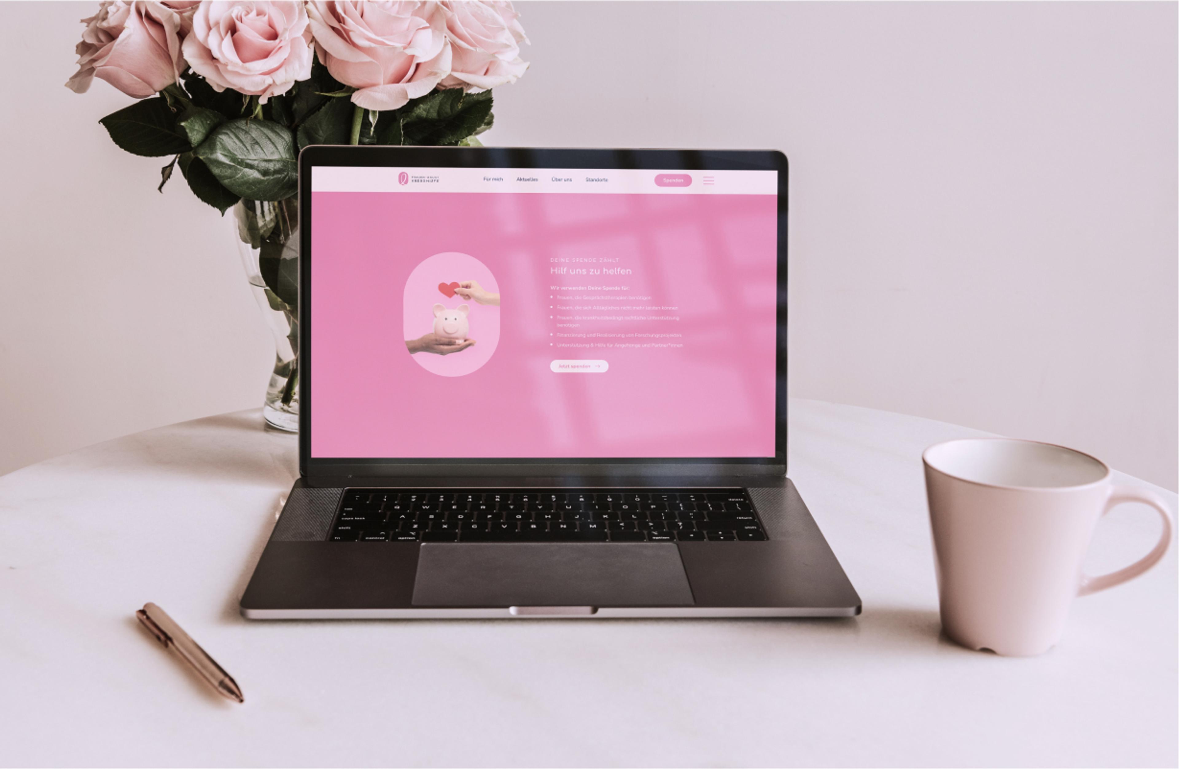Ein Laptop zeigt die Spenden-Seite der Zauberfrauen-Website. Eine Hand hält ein Herz über ein Sparschwein auf rosa Hintergrund.