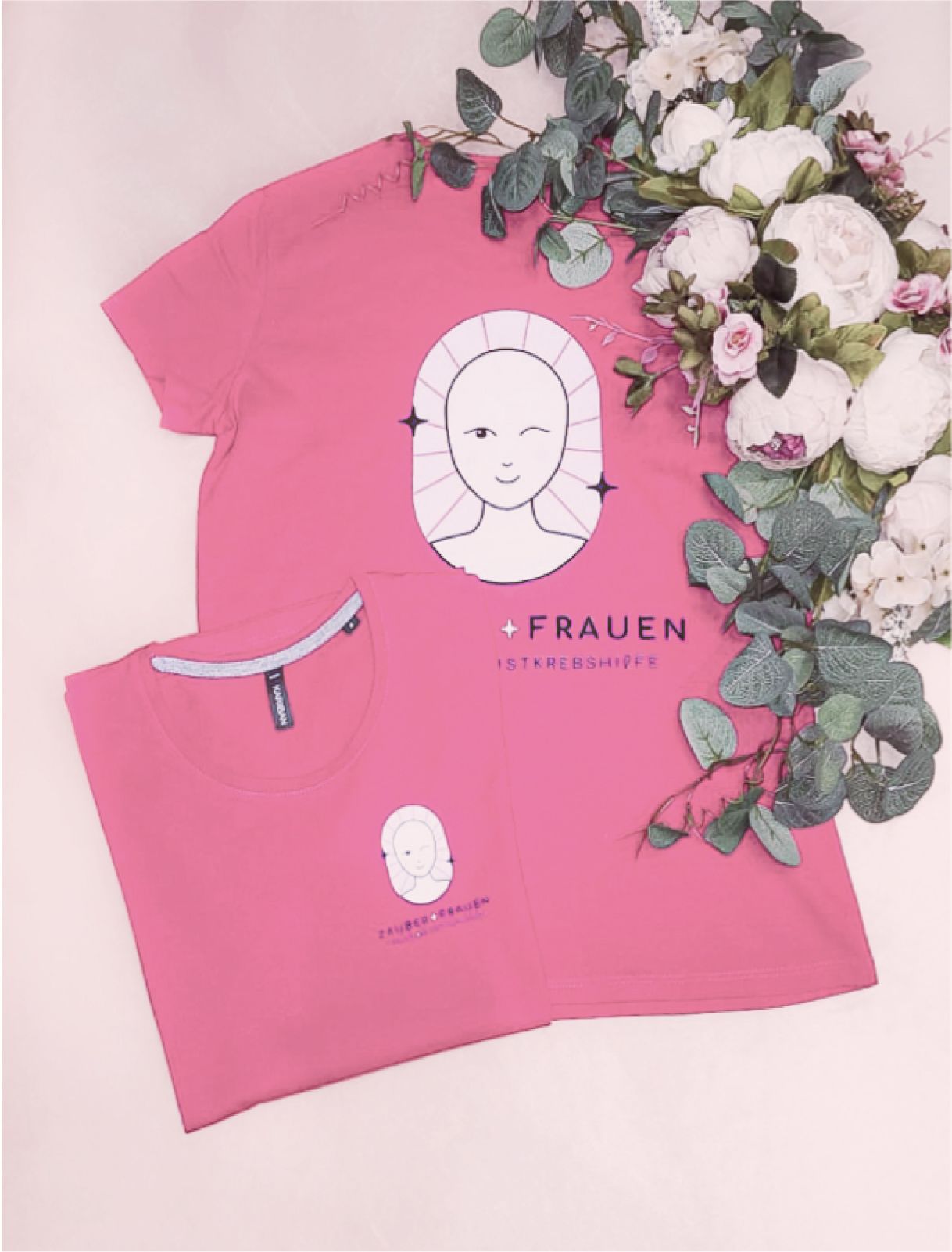 Zwei pinke T-Shirts mit dem Zauberfrauen-Logo, elegant arrangiert mit Blumen. Das Design symbolisiert weibliche Stärke und den Kampf gegen Brustkrebs. - Unerwartet Design