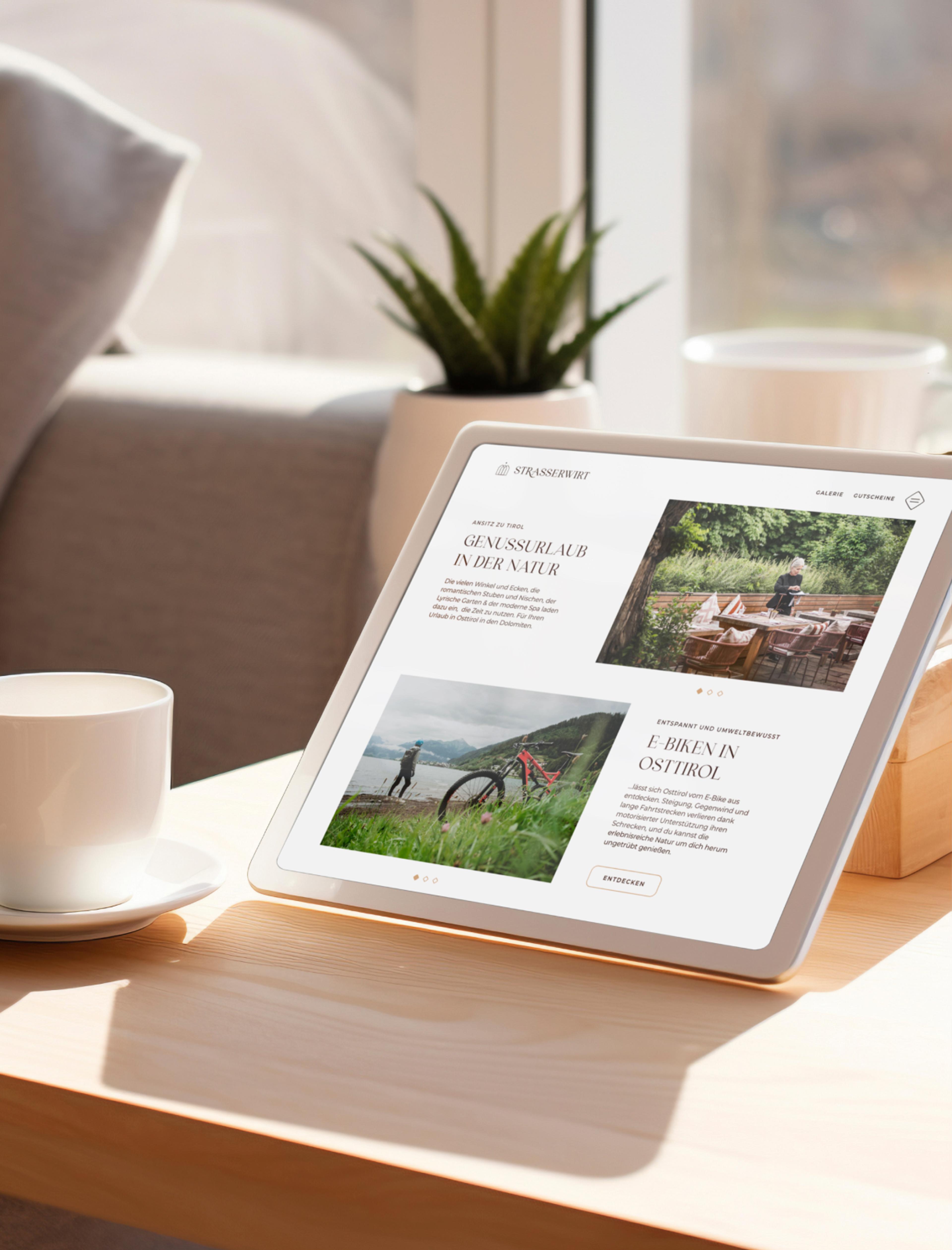 Tablet auf einem Tisch mit Kaffeetasse und Blick aus dem Fenster, zeigt die Strasserwirt-Website mit Informationen zu regionalen Erlebnissen - Unerwartet Design.