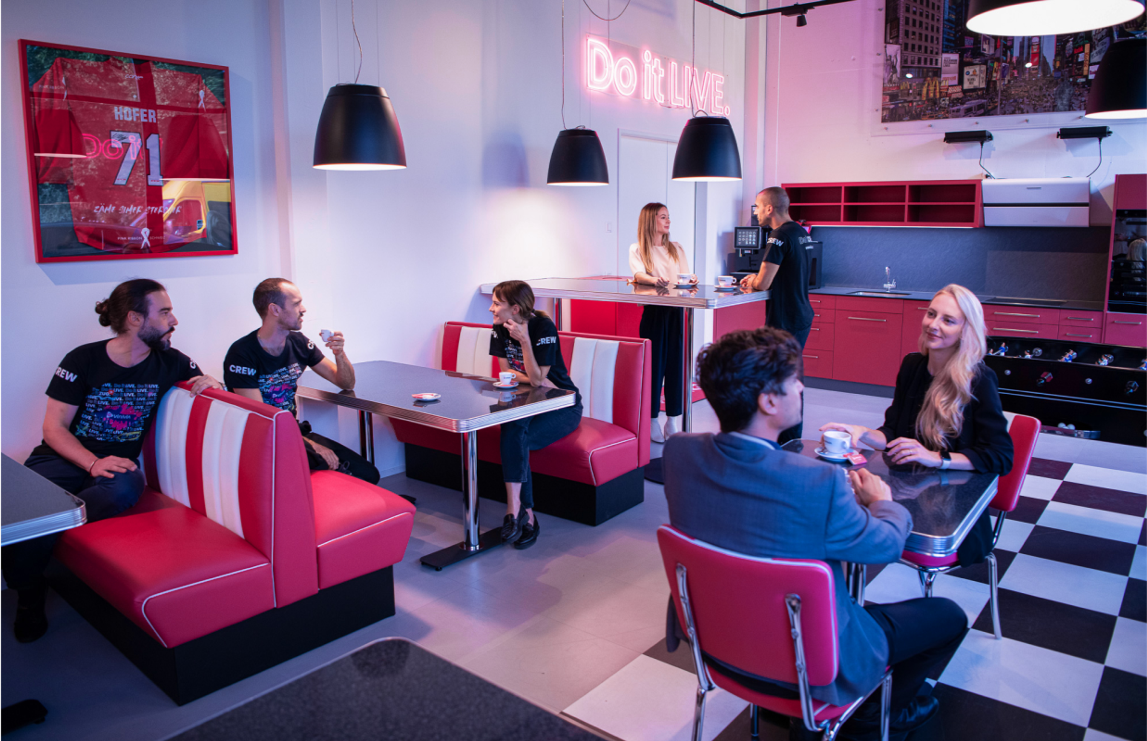 Foto: Vinivia Stylische Küche im Vinivia Office in der Schweiz, gestaltet im Retro-Look mit roten Sitzecken, einer Checkered-Bodenoptik und dem „Do it LIVE“-Neon-Schild – Unerwartet Design