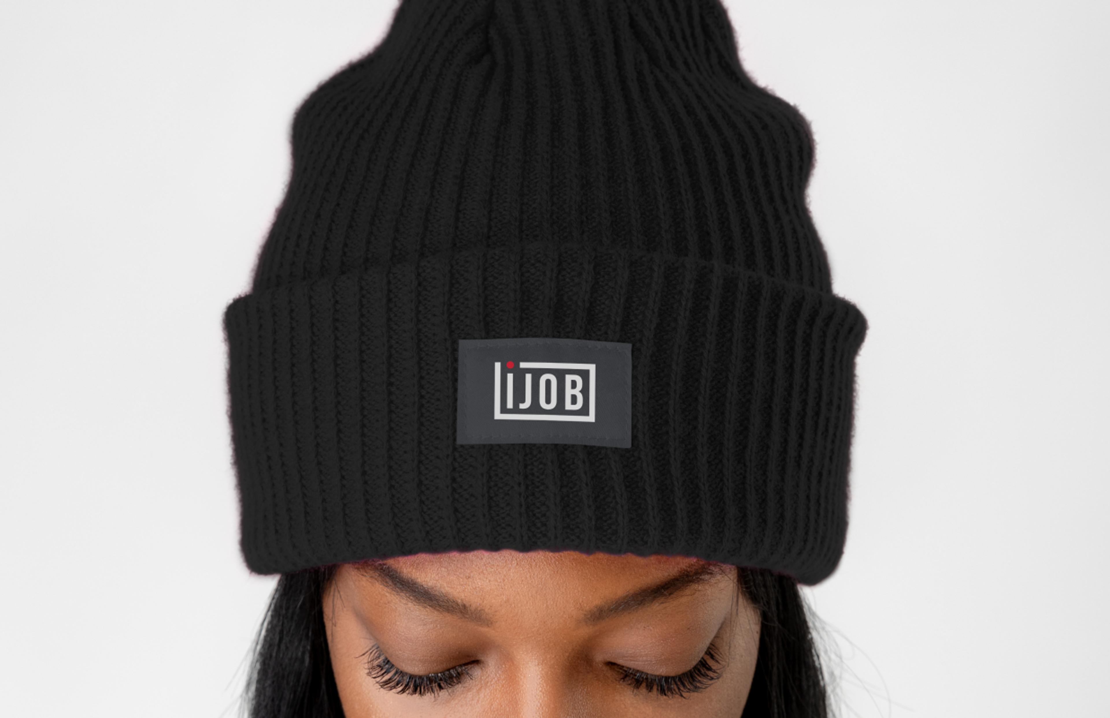 Schwarze Strickmütze mit Ijob-Logo – Eine Person trägt eine schwarze, gerippte Beanie mit einem aufgenähten Ijob-Logo-Patch. Das Logo ist in Weiß mit einem roten Punkt, passend zur Markenidentität.