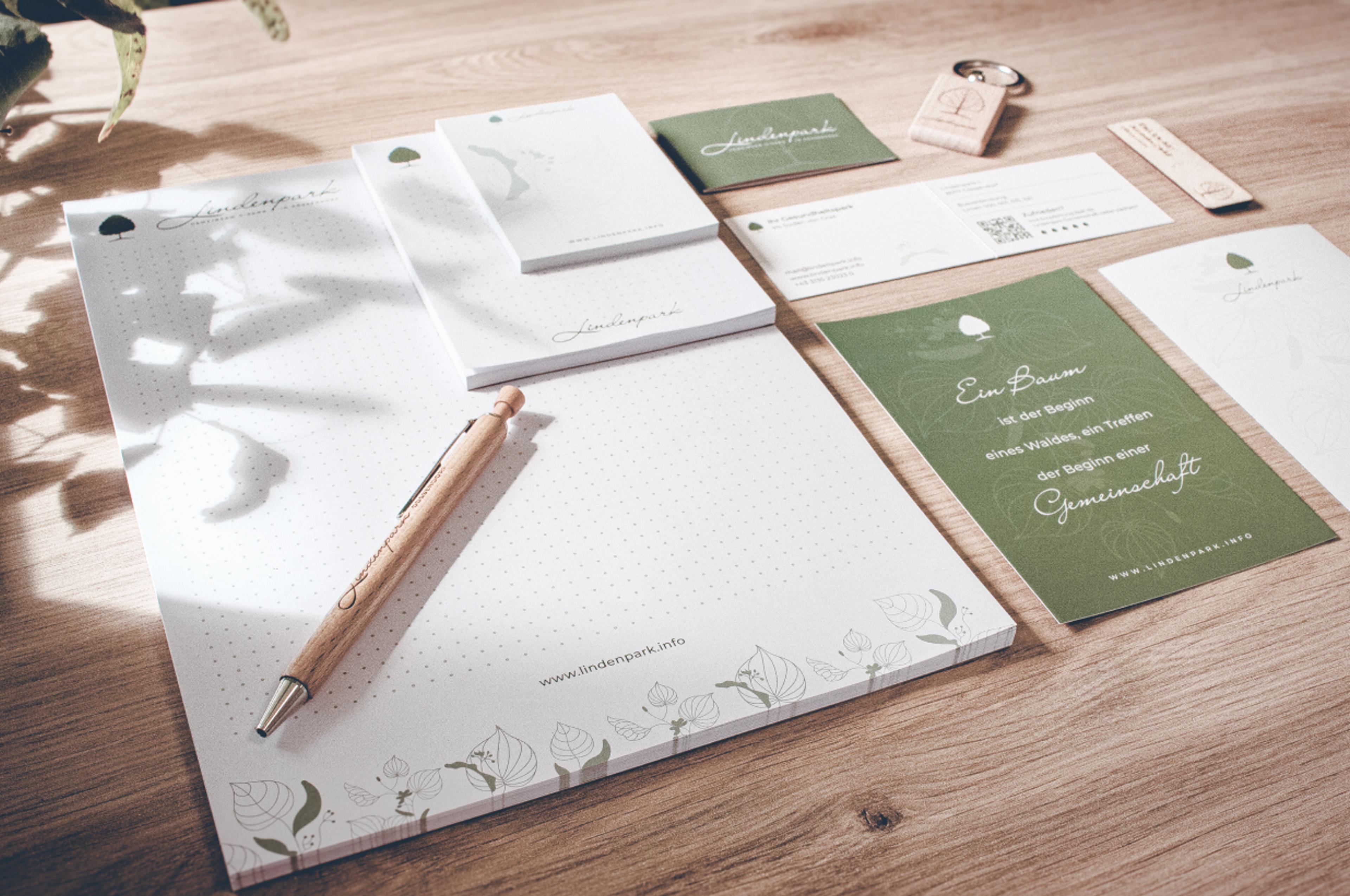 Logo & Grundkonzept BUCHER BRAND MARKETING e.U. Werbematerialien für den Lindenpark, darunter beschriftete Notizblöcke, Visitenkarten und Holzkugelschreiber, gestaltet von Unerwartet Design.